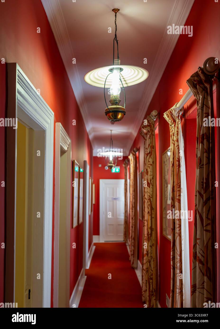 Corridoio rosso interno del castello di Glenveagh nel Glenveagh National Park, contea di Donegal, Irlanda, con lampade a sospensione, tappeto rosso, e tende a motivi geometrici. Foto Stock