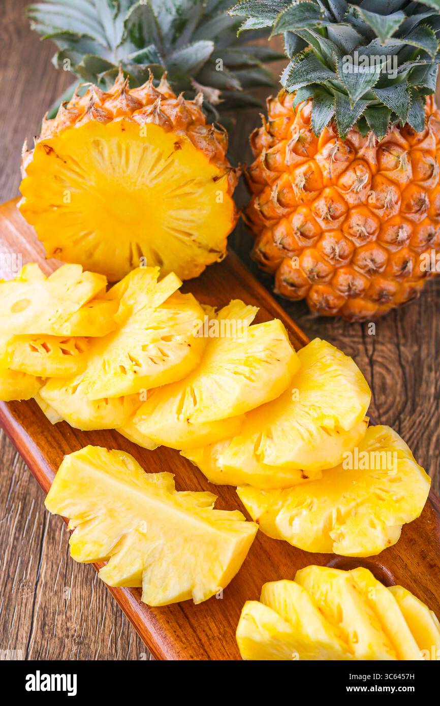 Vista verticale dell'ananas a fette disposto su un tagliere di legno, con un intero ananas posizionato dietro per una vivace presentazione tropicale. Foto Stock