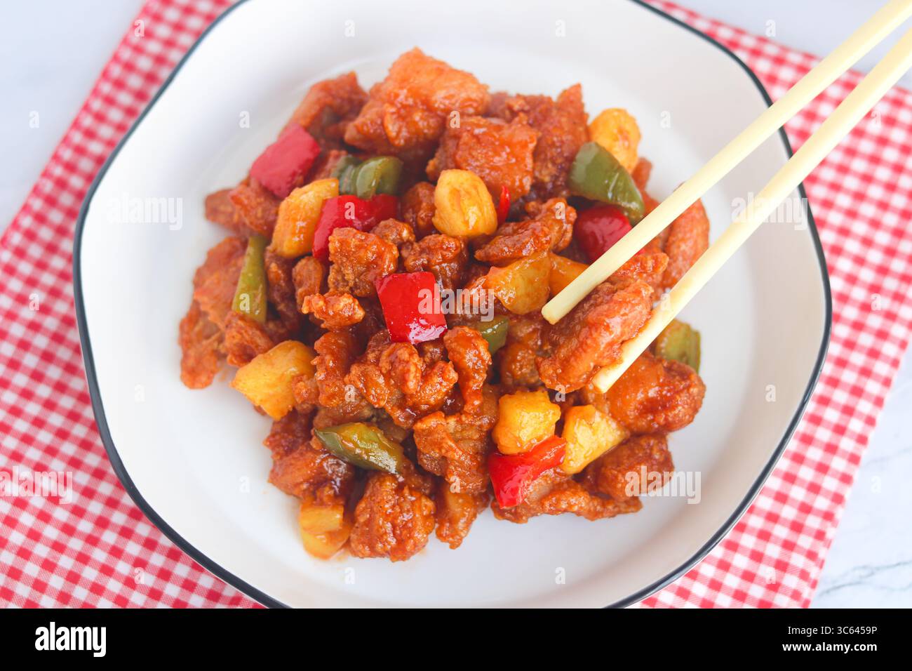 Primo piano di pollo amaro e agrodolce fatto in casa con le bacchette. Decorato con peperoni e pezzi di ananas, servito su un piatto bianco. Foto Stock