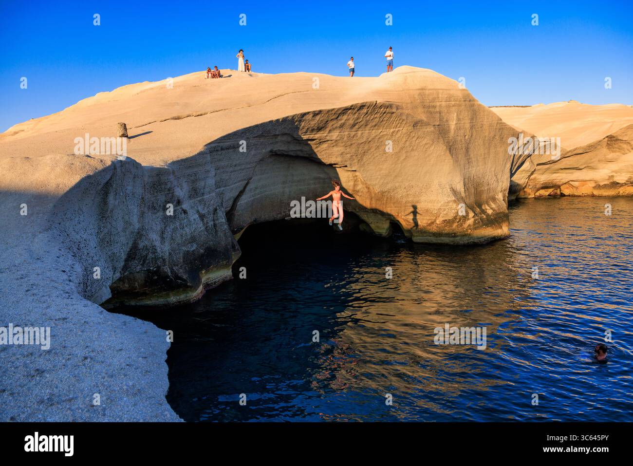 Donna che salta dalla scogliera al mare alla spiaggia di Sarakiniko, Milos, Grecia Foto Stock