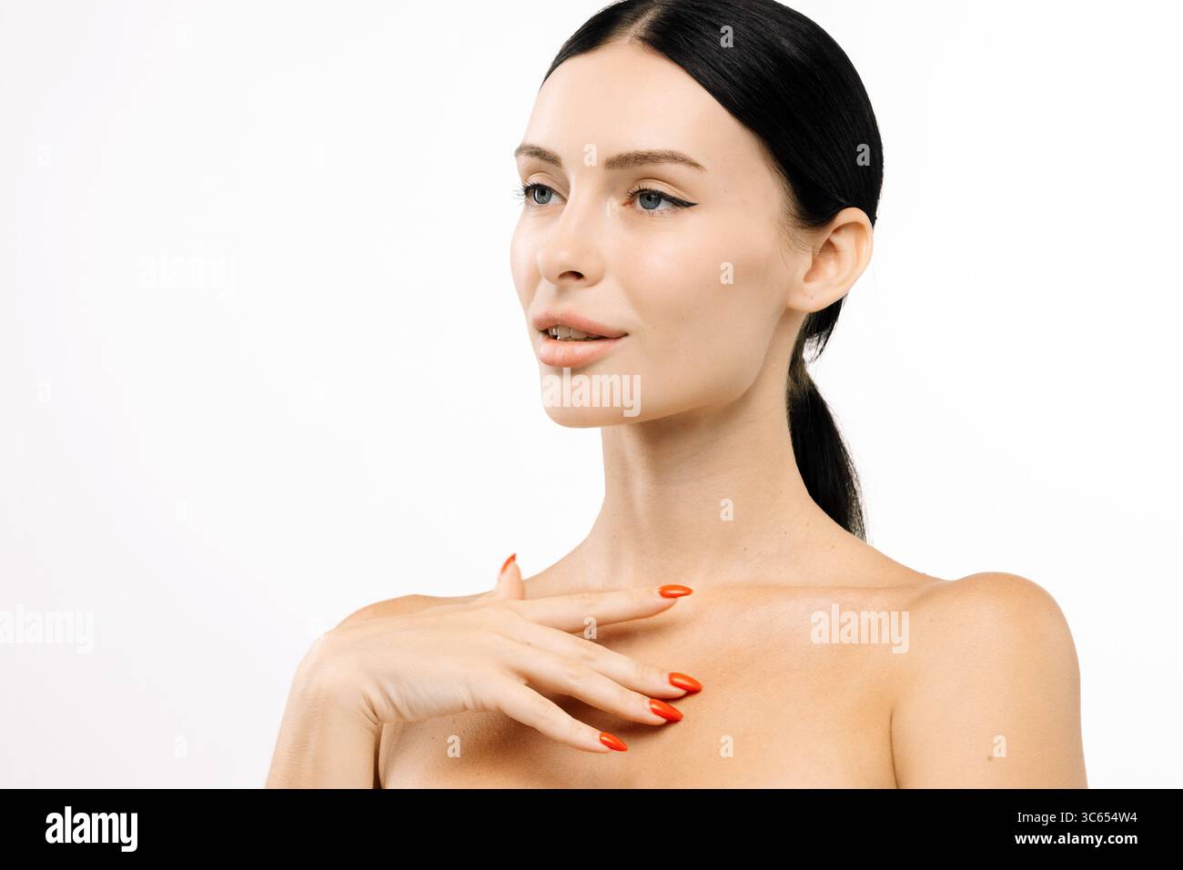 Una donna dalla pelle impeccabile e dalle vivaci unghie rosse poggia elegantemente su uno sfondo bianco pulito, mettendo in risalto la sua bellezza e il suo equilibrio in una splendida bellezza Foto Stock