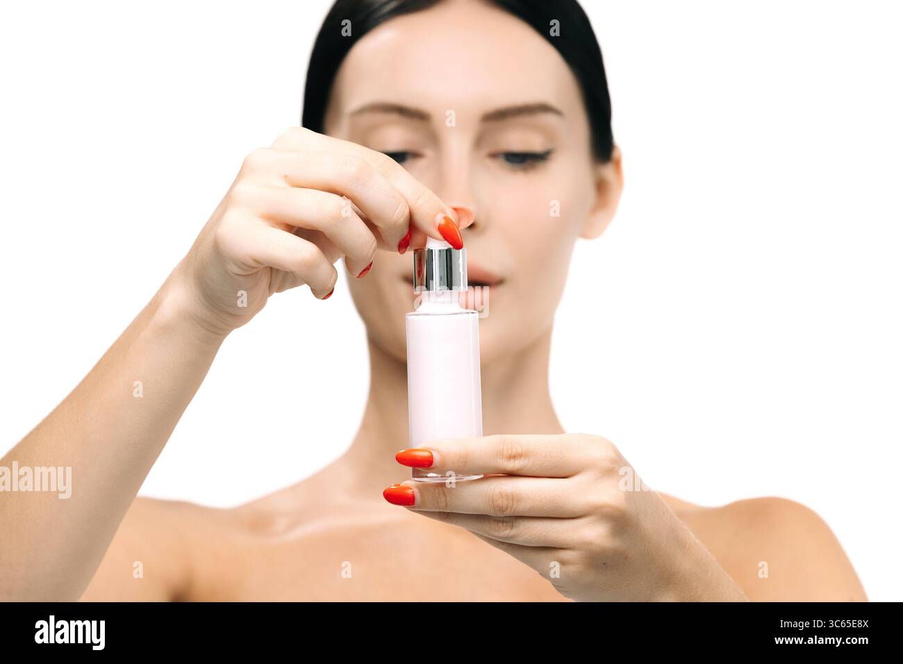 Donna dimostra la routine della cura della pelle tenendo in mano una bottiglia di siero con un contagocce, sottolineando ringiovanimento e bellezza in un ambiente pulito e con luce soffusa Foto Stock