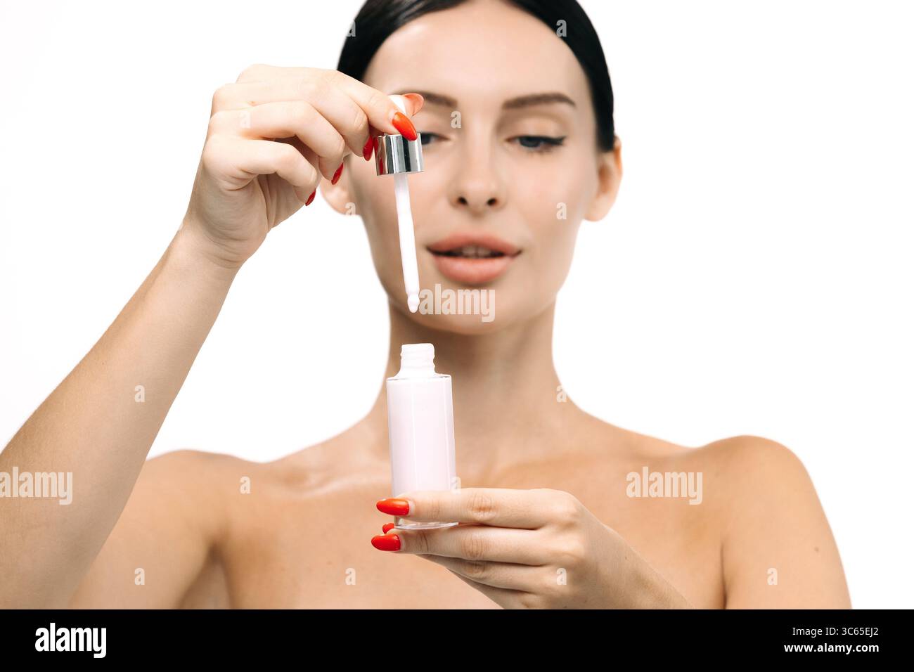 Donna con carnagione radiosa sta applicando siero ringiovanente da un flacone contagocce, evidenziando la routine della cura della pelle e il regime di bellezza per una pelle sana Foto Stock