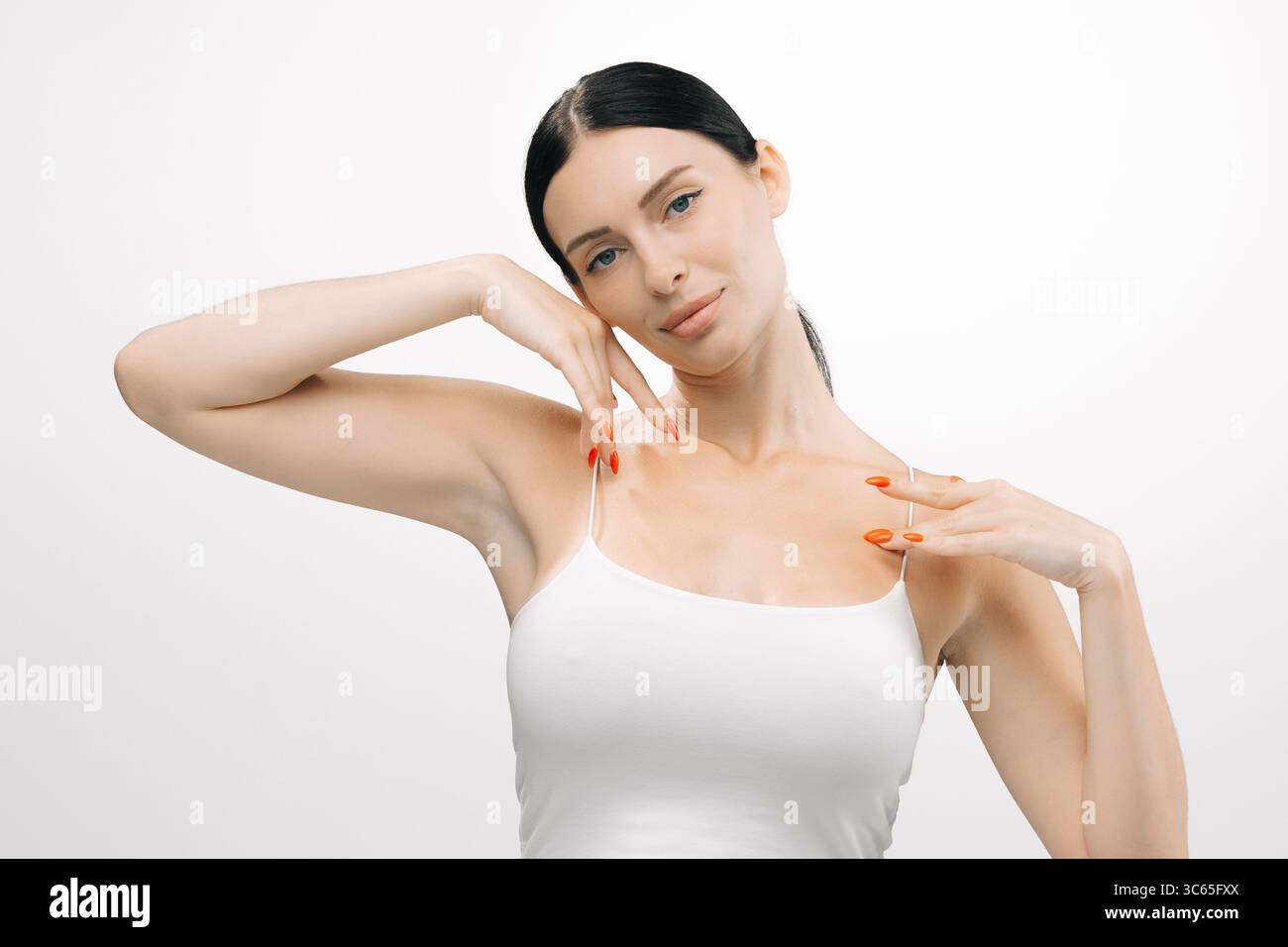 Donna dalla pelle limpida posa elegantemente su uno sfondo bianco, mettendo in risalto la sua impeccabile carnagione e i graziosi movimenti delle mani, che rappresentano la bellezza Foto Stock