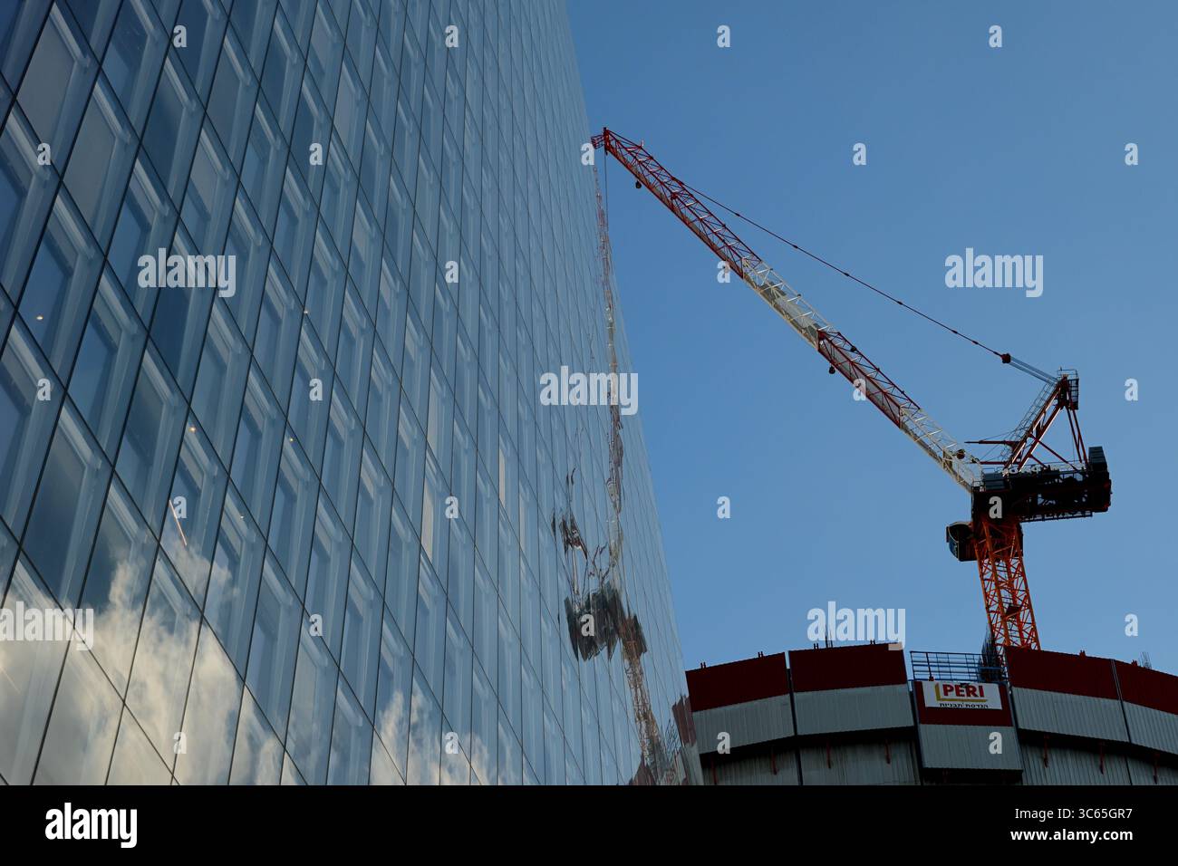 La gru accanto alla torre Azrieli Sarona a Tel Aviv-Jaffa si riflette nella sua facciata sotto il cielo limpido, contrastando forme costruttive con un'architettura elegante. Foto Stock