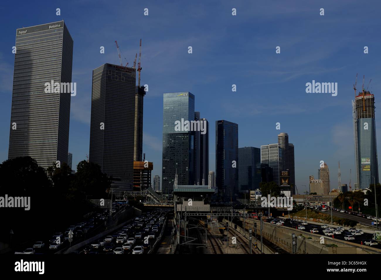 La costruzione di grattacieli a Tel Aviv-Jaffa sorge sopra il paesaggio urbano, evidenziando la struttura in acciaio contro un cielo limpido e l'autostrada trafficata sottostante. Foto Stock
