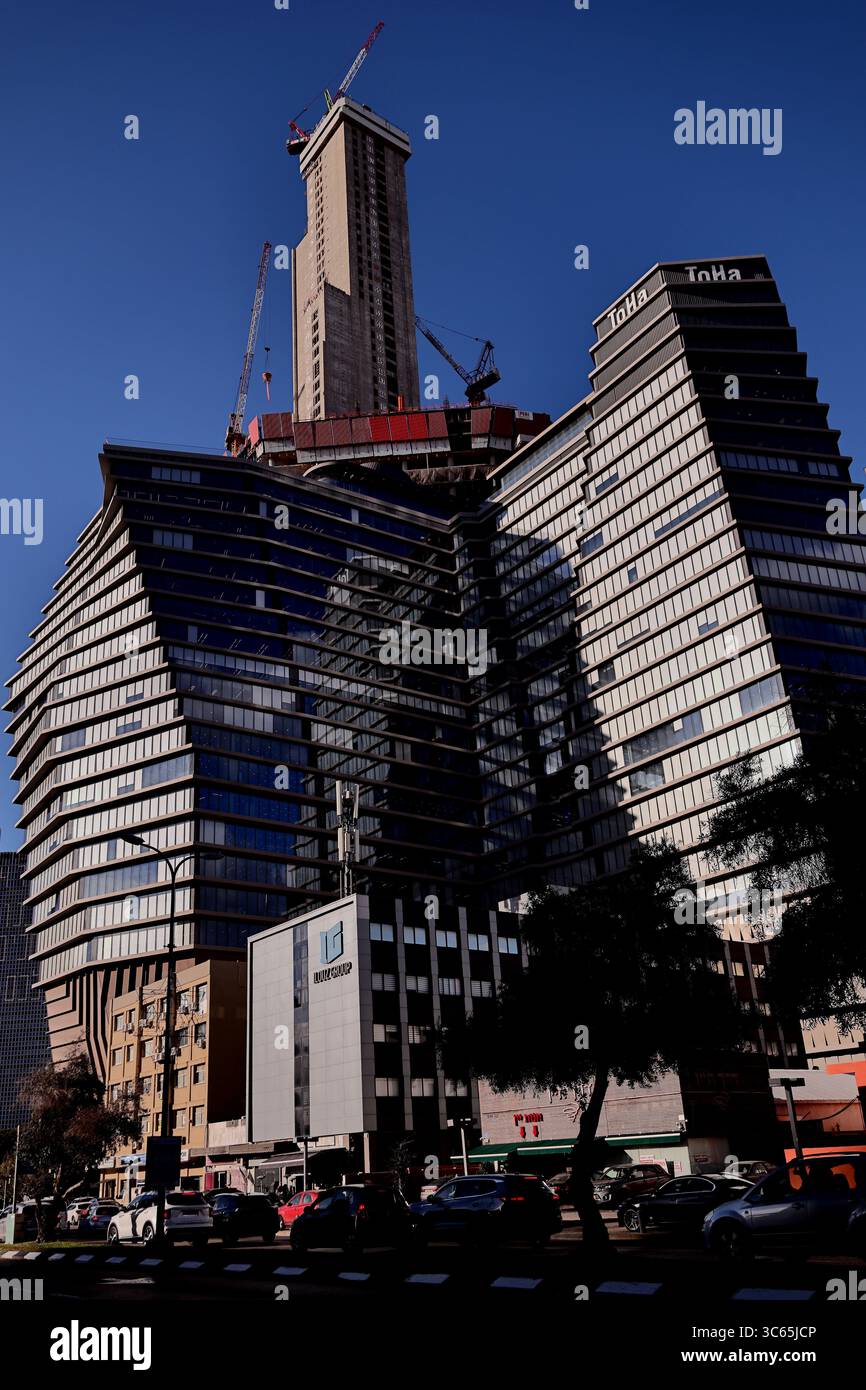 L'imponente costruzione della ToHa Tower 2 a Tel Aviv-Jaffa mette in mostra scintillanti curve di vetro e gru contro un vivace skyline, celebrando l'evoluzione urbana Foto Stock