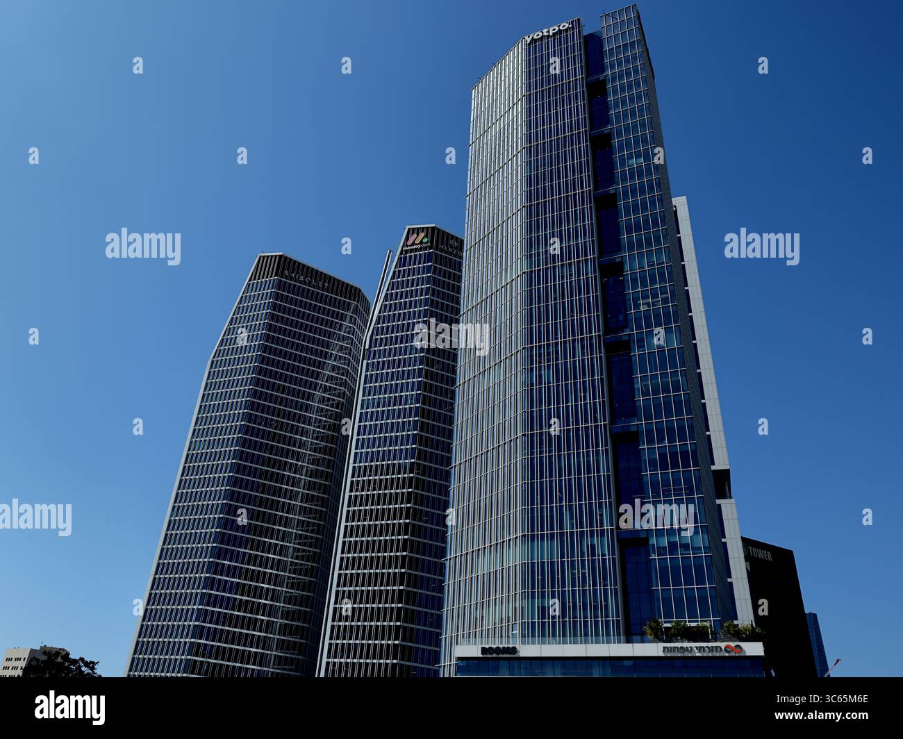 Tre imponenti torri di vetro si innalzano sopra il quartiere aziendale di Tel Aviv-Jaffa, con le loro eleganti facciate geometriche che brillano sottilmente sotto un cielo azzurro. Foto Stock