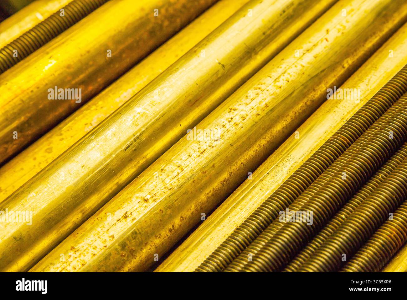 Grandi barre tonde in bronzo e barre filettate in acciaio si trovano su un ripiano, in primo piano. Foto Stock