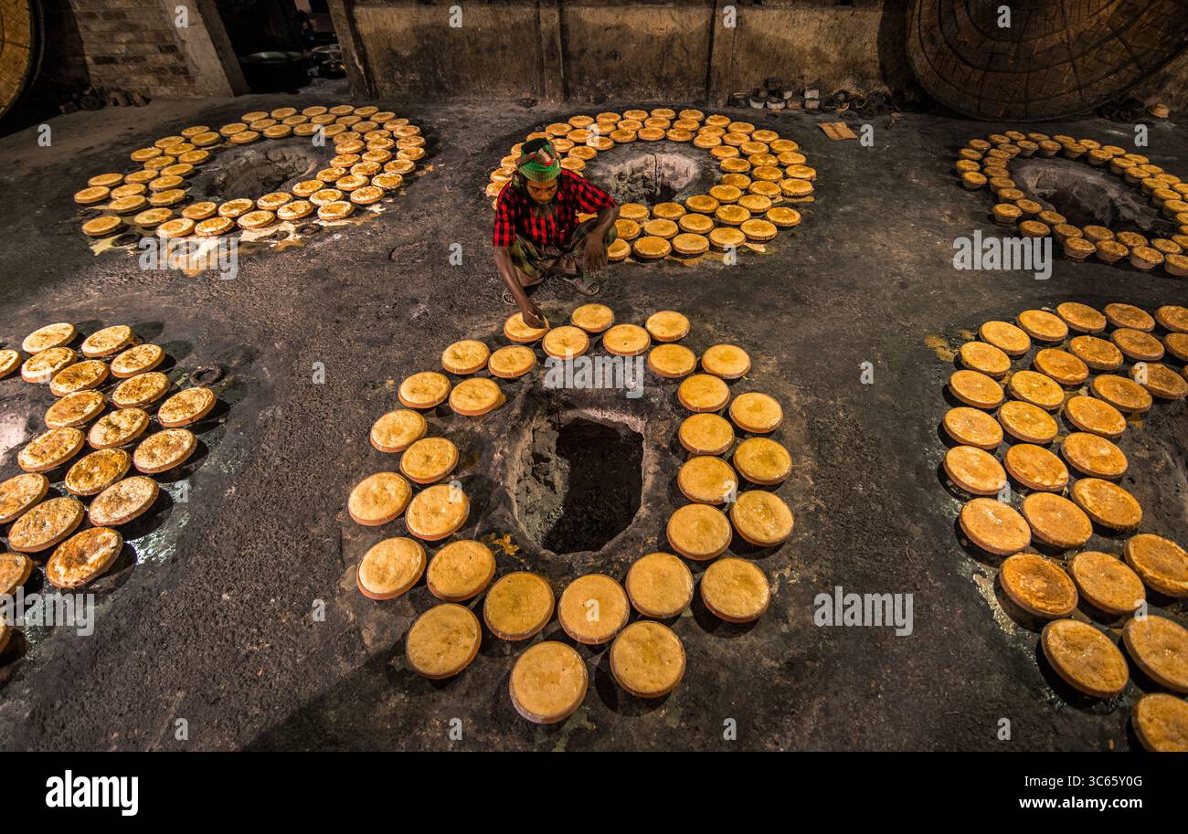 Bogura, Bangladesh - 3 maggio 2020: Vista di un operaio che organizza minuziosamente torte circolari dai toni dorati intorno a pozze scure e macchiate di fuliggine in un pattern ritmico e ripetitivo. Foto Stock