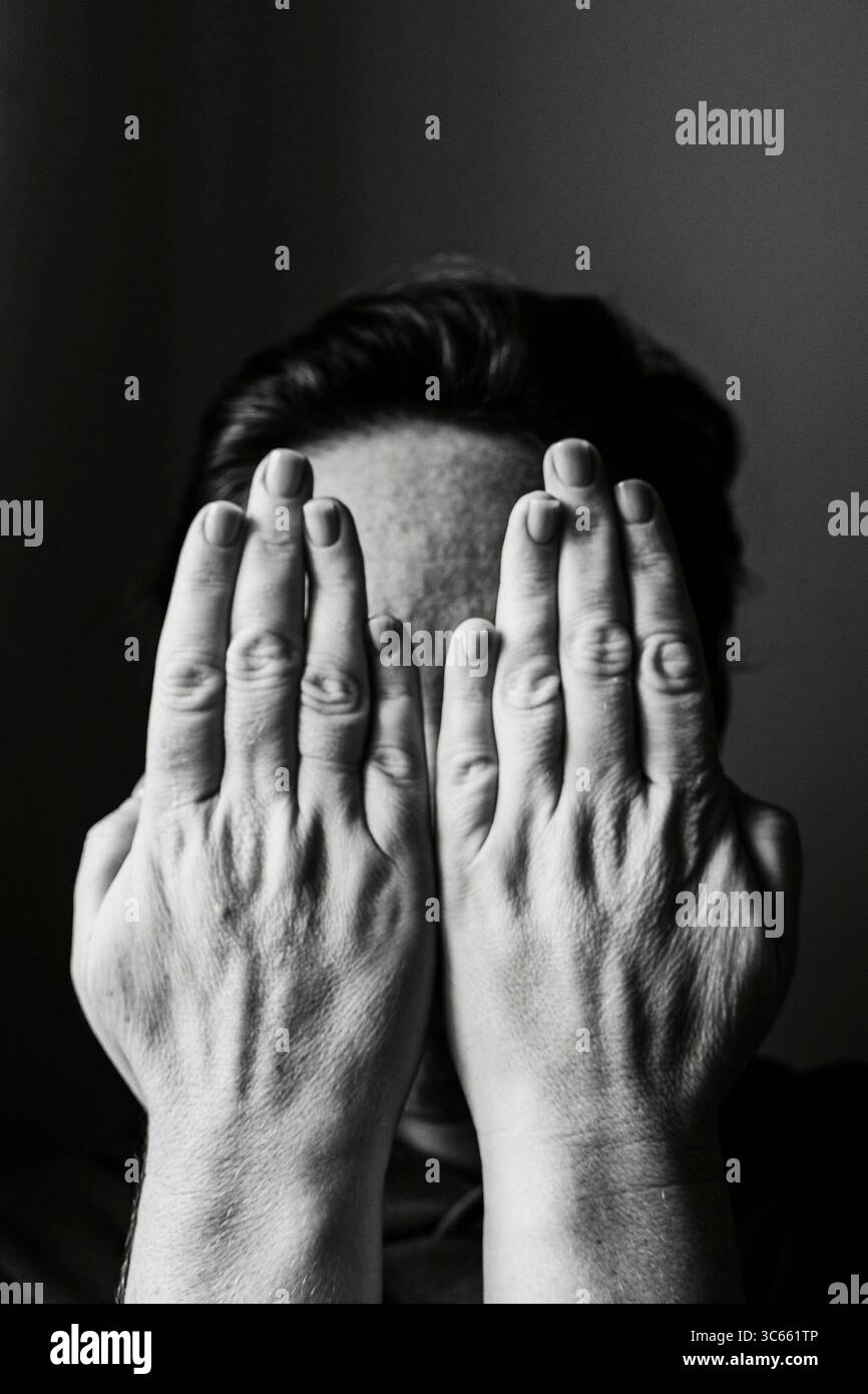 Ritratto ravvicinato di una donna che nasconde il volto con le mani, trasmette emozioni di timidezza o introspezione. La composizione in bianco e nero viene evidenziata Foto Stock