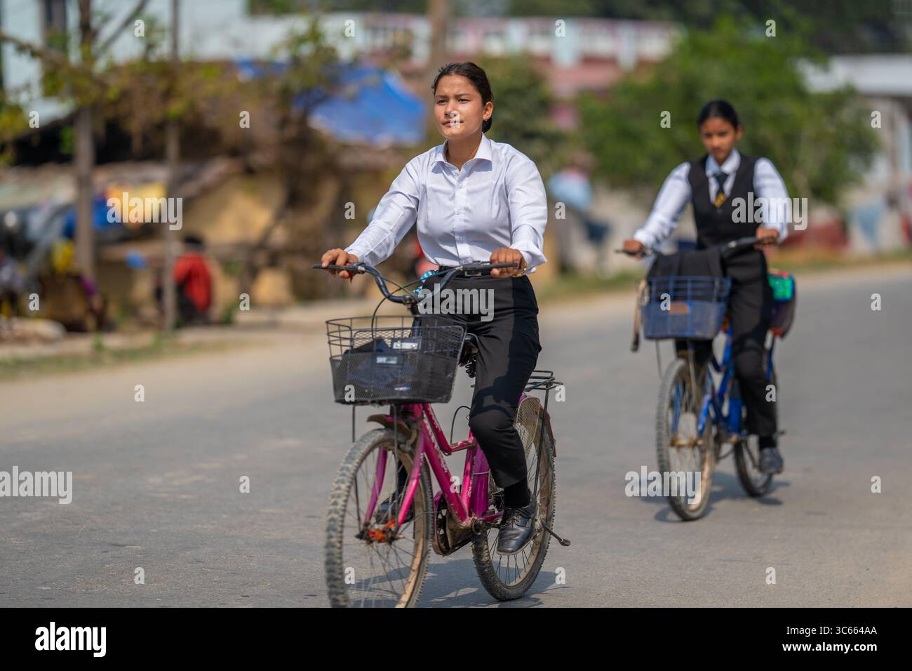 Dhangadhi, Nepal - 03 marzo 2023: Vista di due giovani donne in abbigliamento formale che pedalano lungo una strada soleggiata, le loro moto gettano lunghe ombre sull'asfalto, incarnando l'energia giovanile. Foto Stock