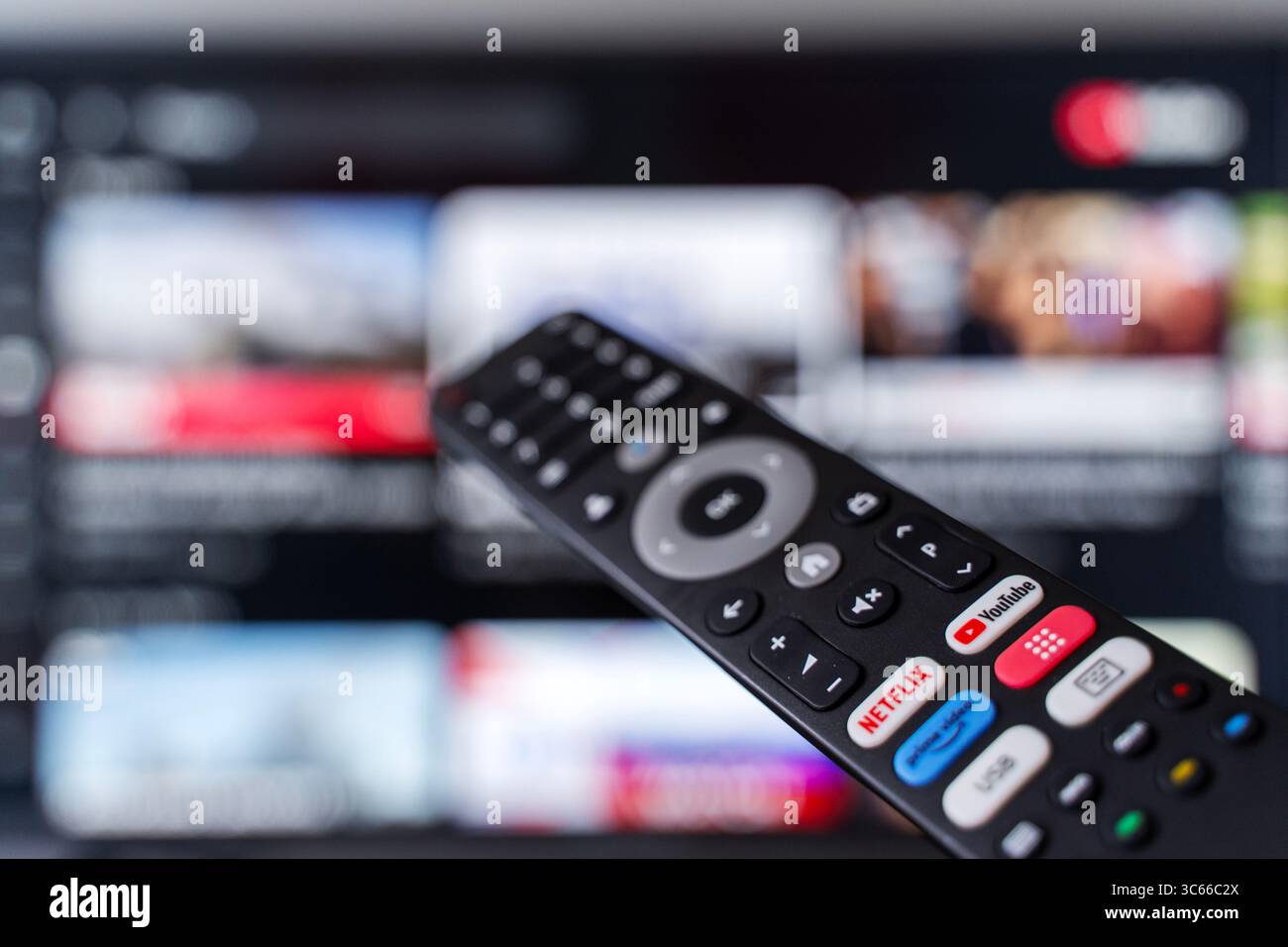 Tbilisi, Georgia - 2 luglio 2025: Foto ravvicinata di un telecomando smart TV con pulsanti dedicati per piattaforme di streaming popolari come Netflix, YouTube e Amazon prime, con uno schermo televisivo sfocato sullo sfondo. Rappresenta il consumo dei moderni media digitali, i servizi basati su abbonamento e l'intrattenimento on demand. Ideale per contenuti tecnologici, in streaming, binge-watching o media lifestyle. Foto Stock