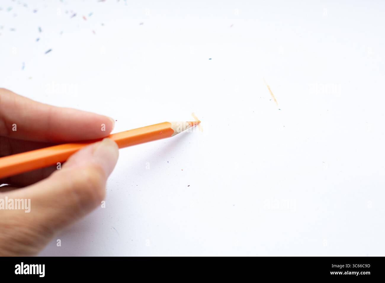 Una persona tiene in mano una matita arancione su un pezzo di carta Foto Stock