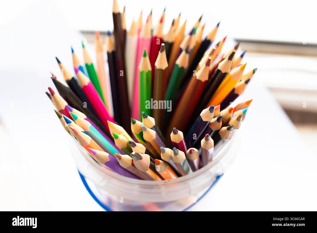 Un secchio pieno di matite colorate appoggiate su un tavolo Foto Stock