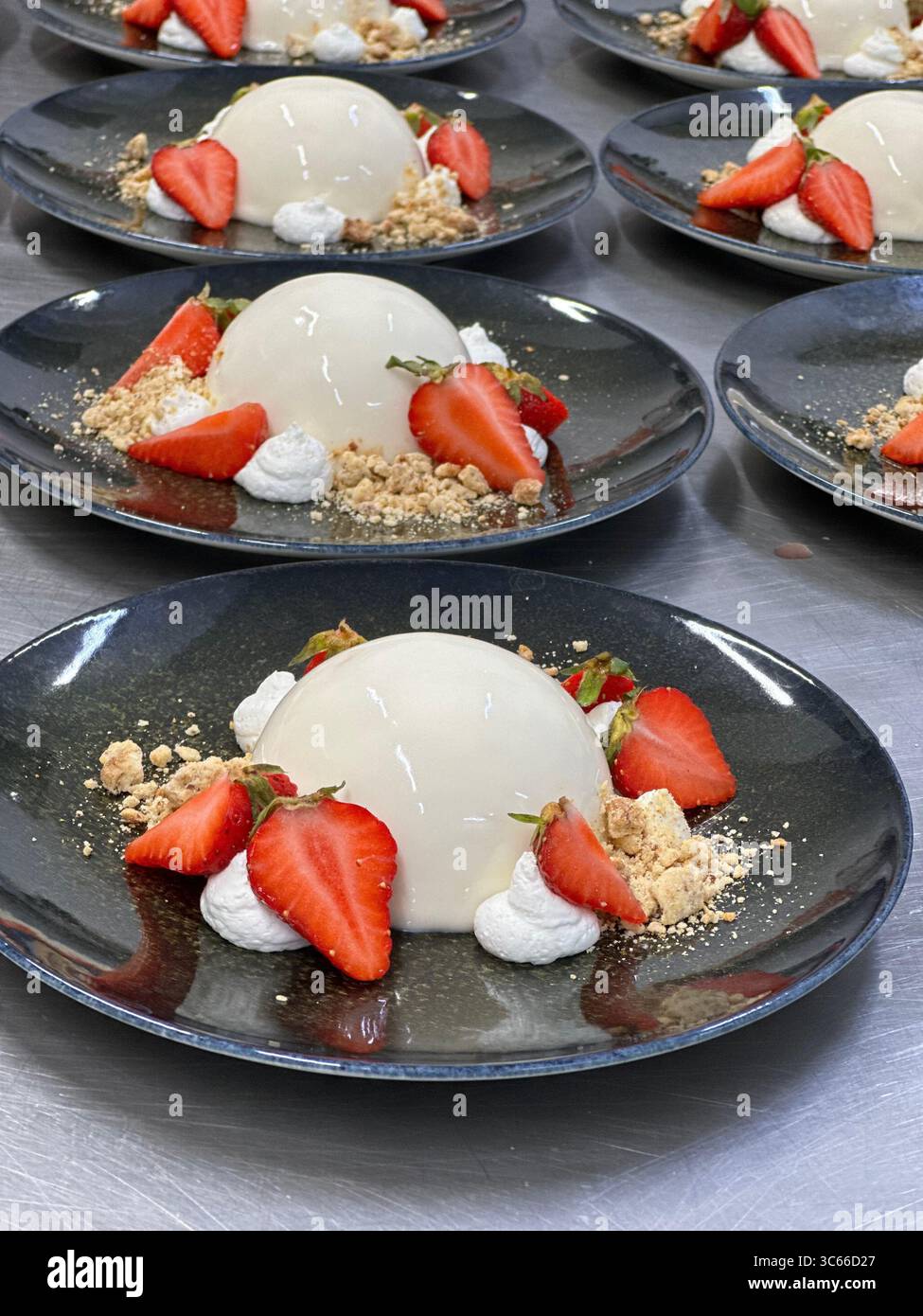 Panna cotta con fragole fresche su un piatto nero da vicino Foto Stock