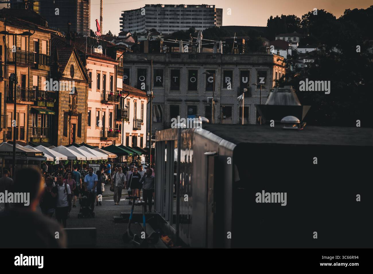Porto, Portogallo - 17 giugno 2022: Vista del vivace quartiere di Ribeira, dove il caldo bagliore del tramonto bacia il fiume Douro e gli edifici storici, gettando lunghe ombre sulla folla. Foto Stock