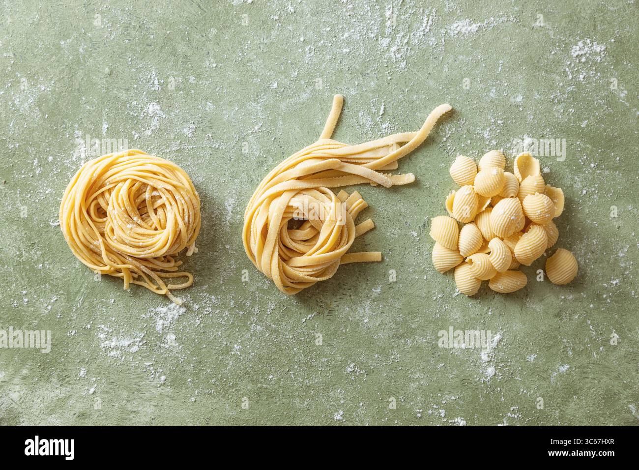 Varietà di pasta cruda fatta in casa fresca. Spaghetti, tagliatelle e conchiglie di pasta su una superficie di lavoro infarinata. Foto Stock