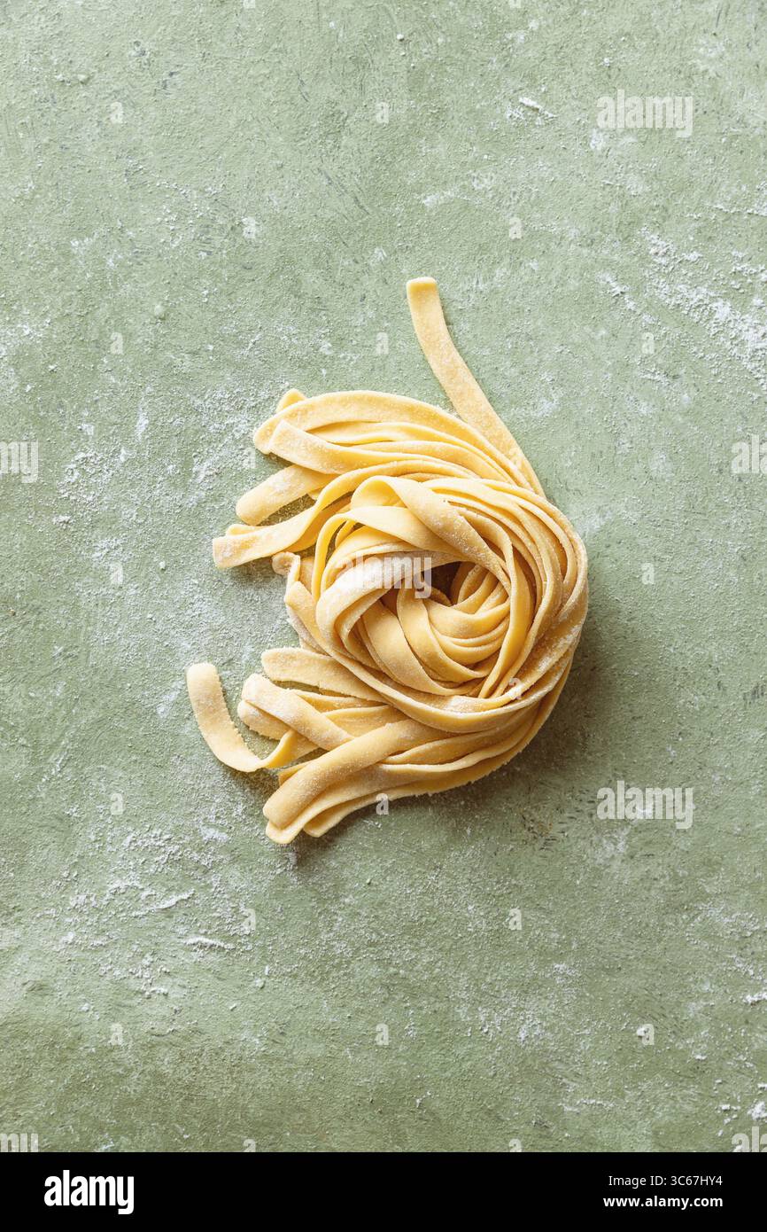 Tagliatelle fresche crude fatte in casa su una superficie di lavoro infarinata. Foto Stock