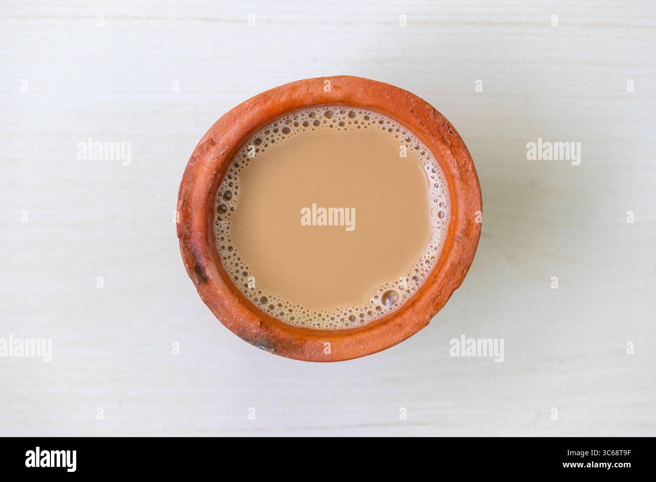 Vista dall'alto di una tazza di tè al latte o di Dudh Cha in una tradizionale tazza di argilla, appoggiata su una superficie di legno chiaro. Foto Stock