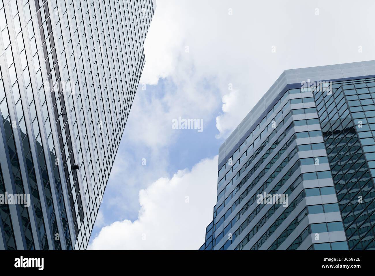 Scena urbana con grattacieli di vetro torreggianti con uno sfondo di cielo blu e nuvole, che esaltano l'eleganza architettonica e l'atmosfera urbana Foto Stock