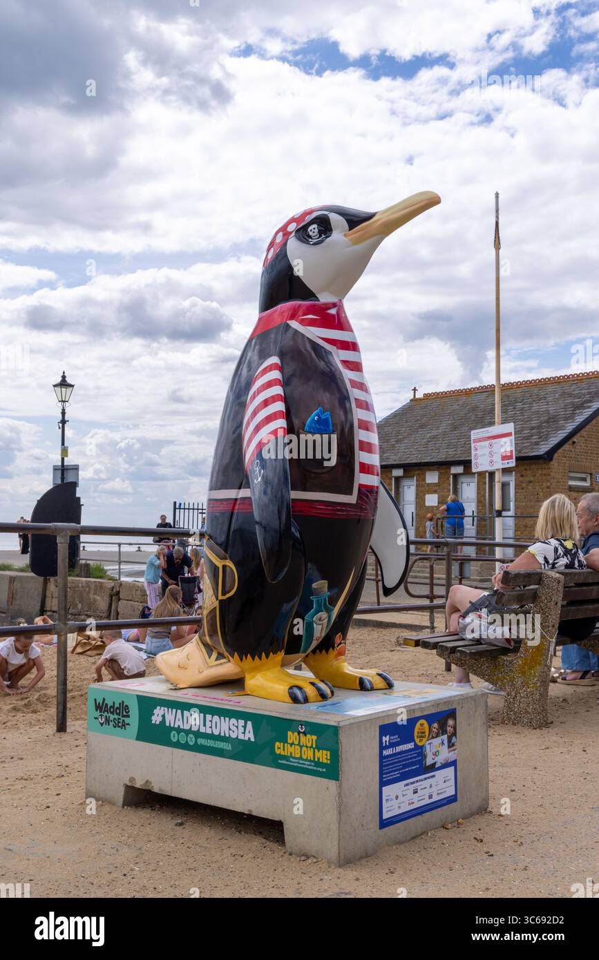 Statua del pinguino a tema pirata in mostra pubblica a Leigh-on-Sea, Essex, Regno Unito. Parte di un percorso artistico sul mare con visitatori ed edifici sullo sfondo. Foto Stock