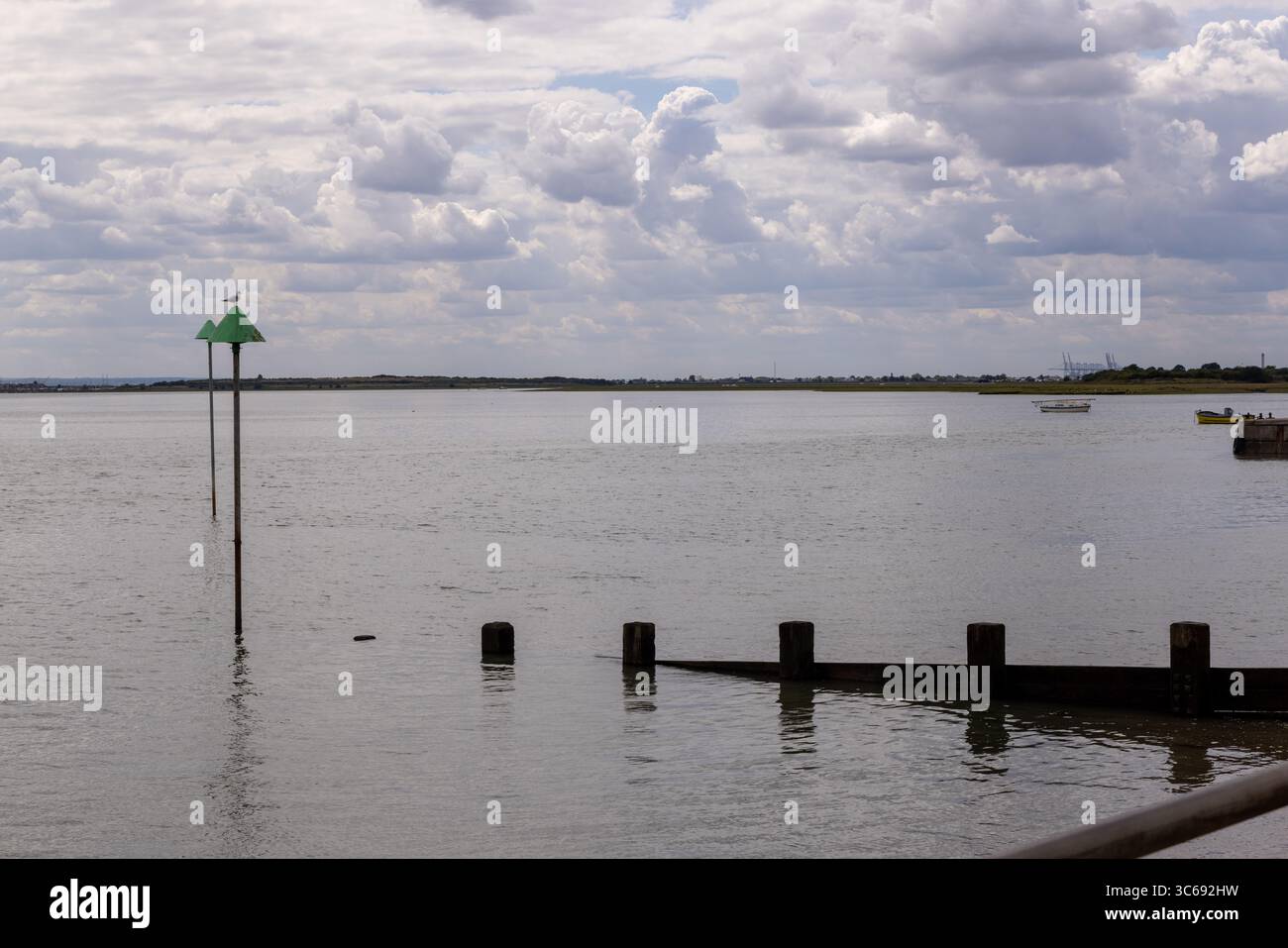 Groynes si estendeva nell'estuario del Tamigi a Leigh-on-Sea, Essex, Inghilterra. Difese costiere con acque calme, indicatori di navigazione e cielo nuvoloso. Foto Stock