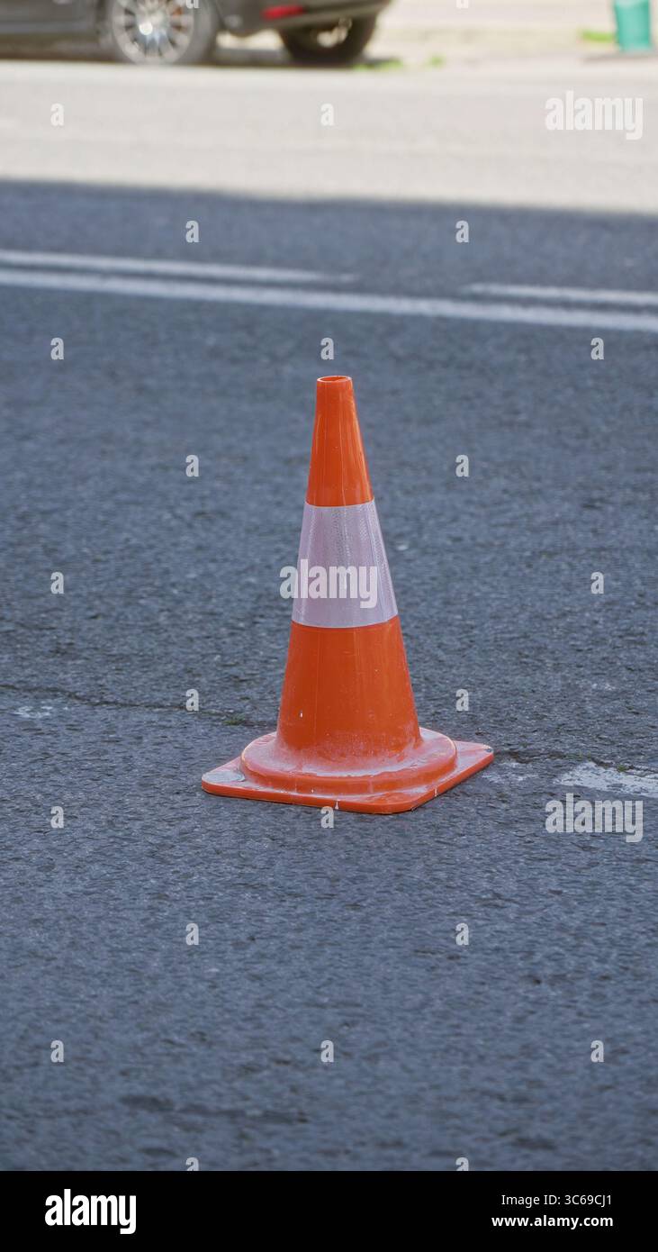 Cono stradale arancione su una strada soleggiata all'aperto con cieli limpidi, che enfatizza la sicurezza stradale e le infrastrutture urbane in un ambiente urbano. Foto Stock