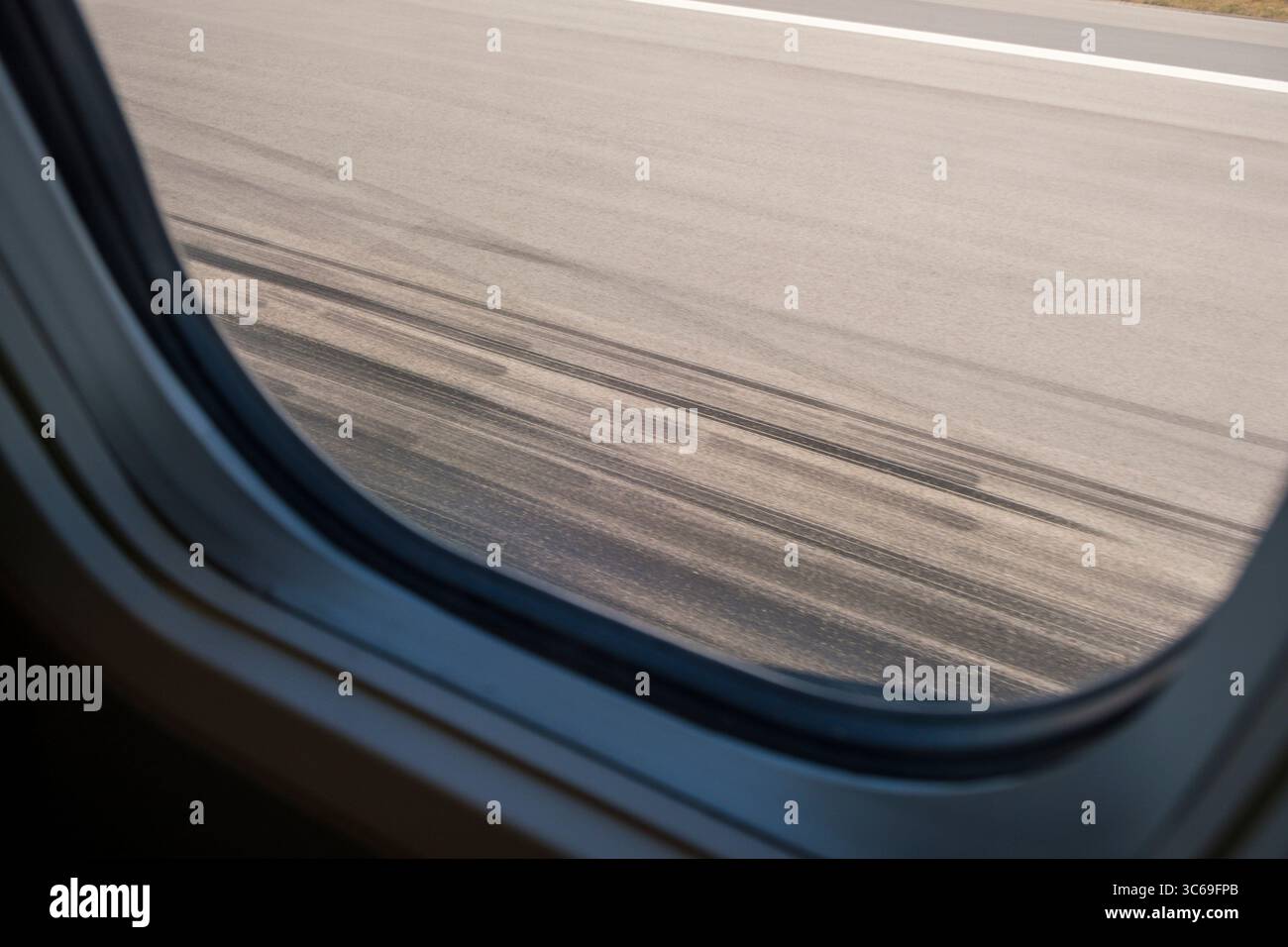 Vista dal finestrino di un aeromobile al decollo con segni di scorrimento neri sulla pista lasciata dagli altri pneumatici dell'aeromobile. Foto Stock