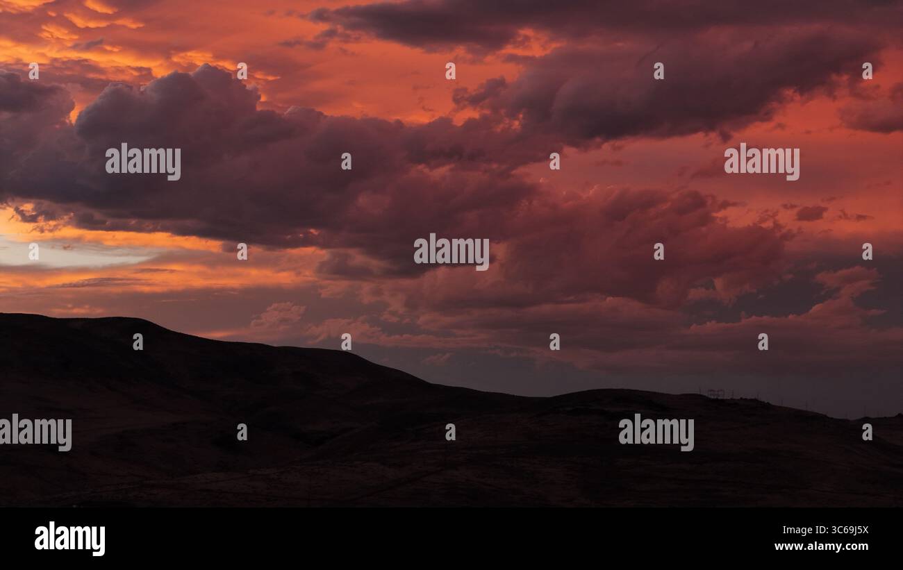 La vista aerea di un tramonto sereno dipinge il cielo con sfumature di fuoco sopra le colline scure e ondulate che gettano ombre lunghe, Reno, Nevada, Stati Uniti. Foto Stock