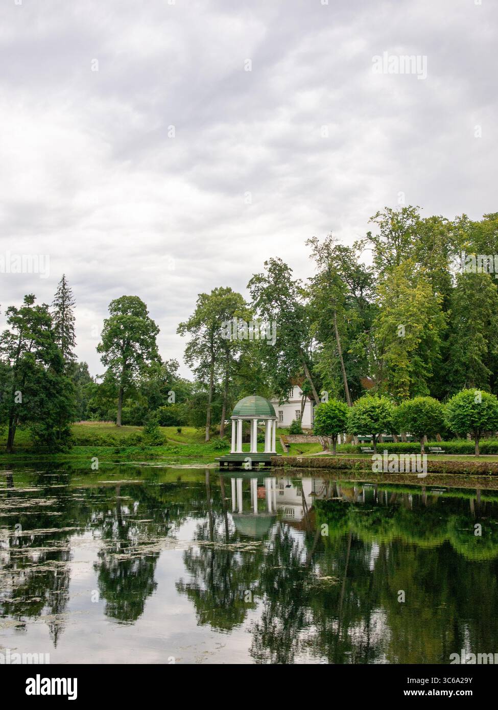 Un padiglione classico nei giardini paesaggistici del parco di Palmse Manor, riflesso nello stagno ornamentale circondato da alberi maturi e da un paesaggio formale. Foto Stock