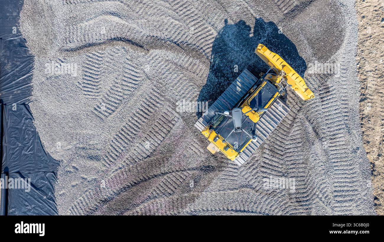 Antenna di un drone sopra un bulldozer che lavora in cantiere, monitora e osserva i progressi della costruzione. Uso della tecnologia su una costruzione Foto Stock