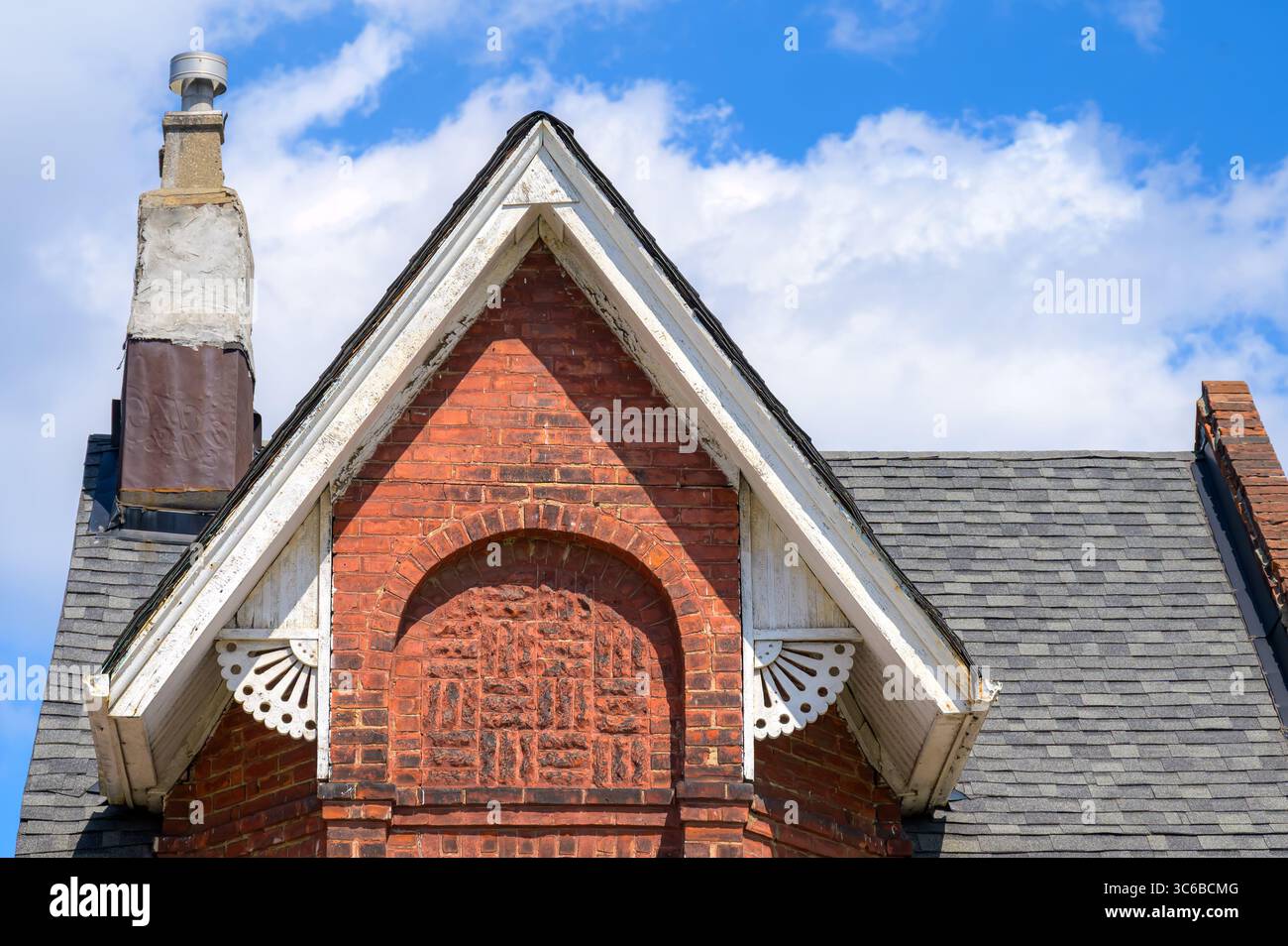 Un ripido tetto a tetto spiovente con finiture in legno ornato incornicia un arco in mattoni su una casa vittoriana rossa, con un camino intempestivo ai suoi lati. Foto Stock