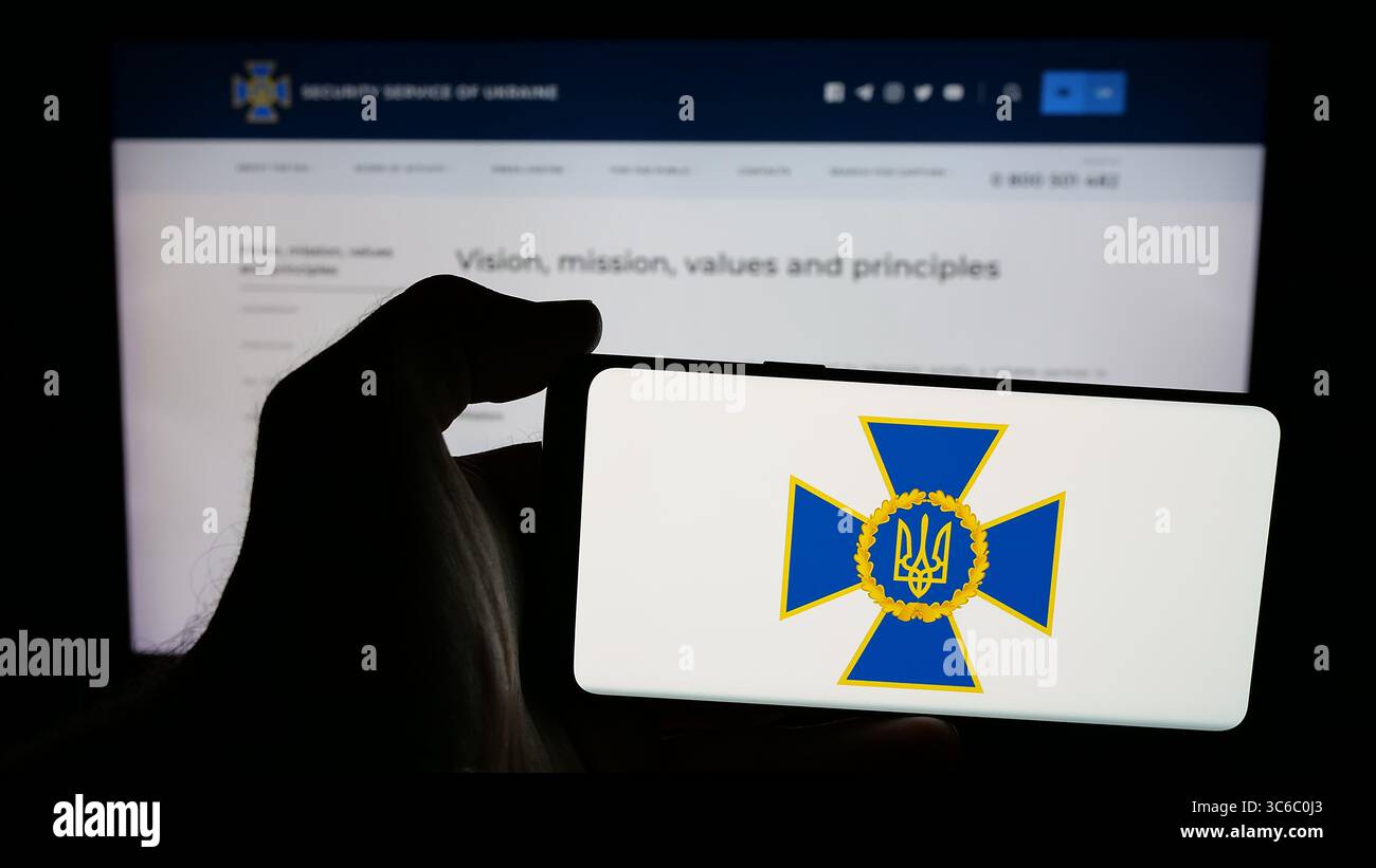 Stoccarda, Germania - 06-18-2025: Persona che detiene un telefono cellulare con logo del servizio di sicurezza Sluzhba Bezpeky Ukrainy SBU sullo schermo di fronte alla pagina web. Foto Stock