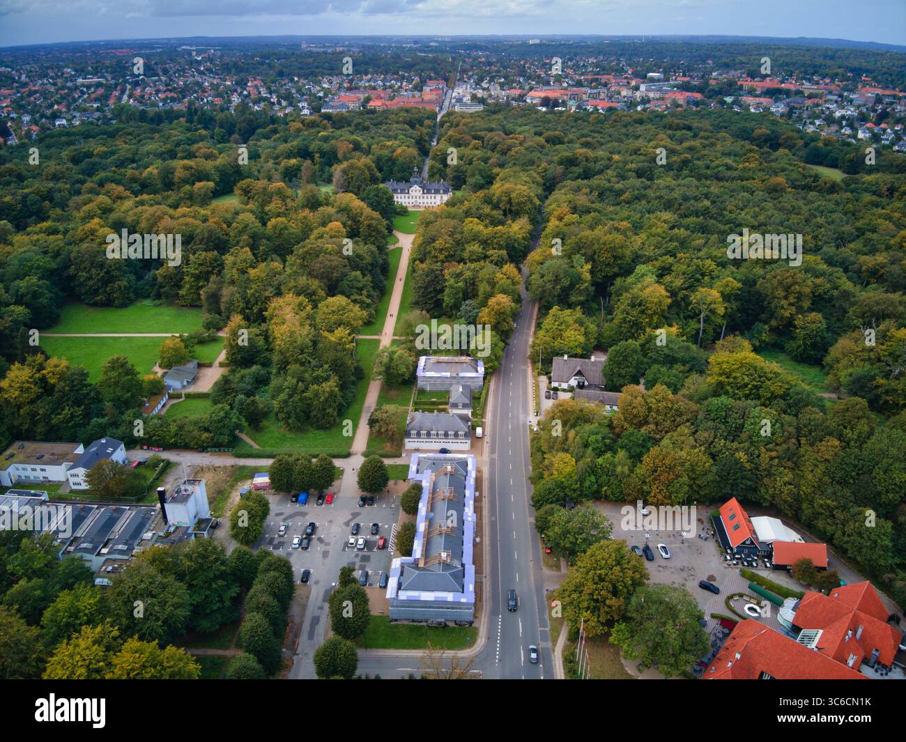 Veduta aerea di una strada che attraversa una fitta foresta, con edifici e parcheggi che aggiungono un tocco di civiltà, Gentofte, Danimarca. Foto Stock