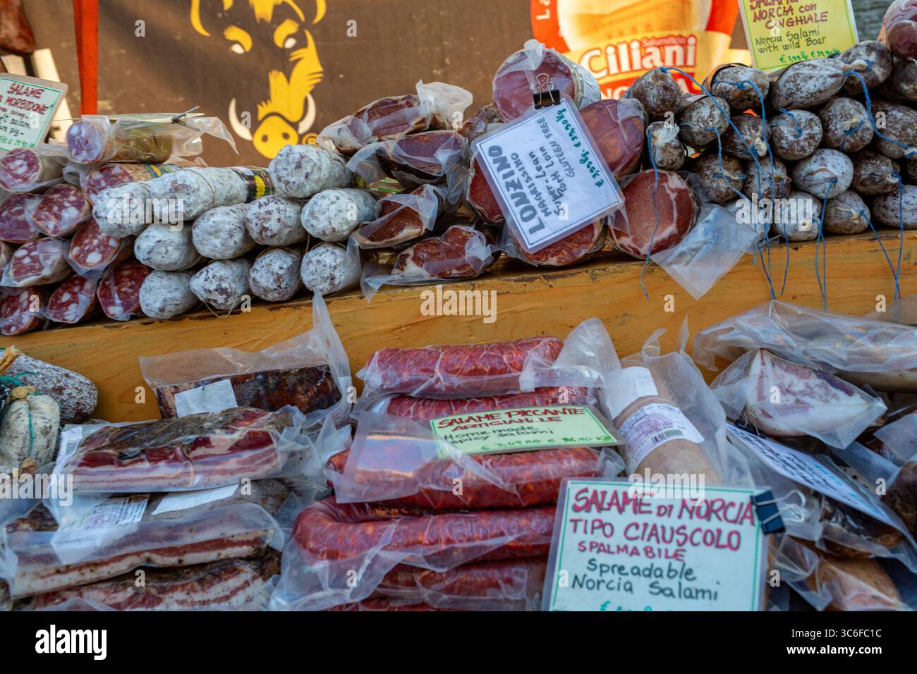 Una vivace esposizione di salumi assortiti su una stalla di legno, con vari salumi e salsicce con etichette, che mettono in risalto la cultura gastronomica tradizionale Foto Stock