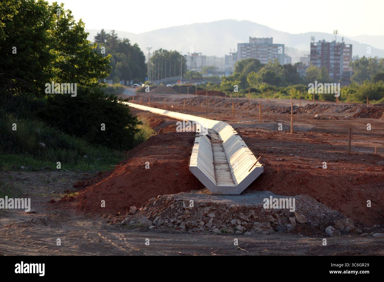 Una nuova linea di grandi canali di drenaggio in calcestruzzo prefabbricato si estende attraverso la terra rossa, formando parte di un nuovo progetto infrastrutturale urbano Foto Stock