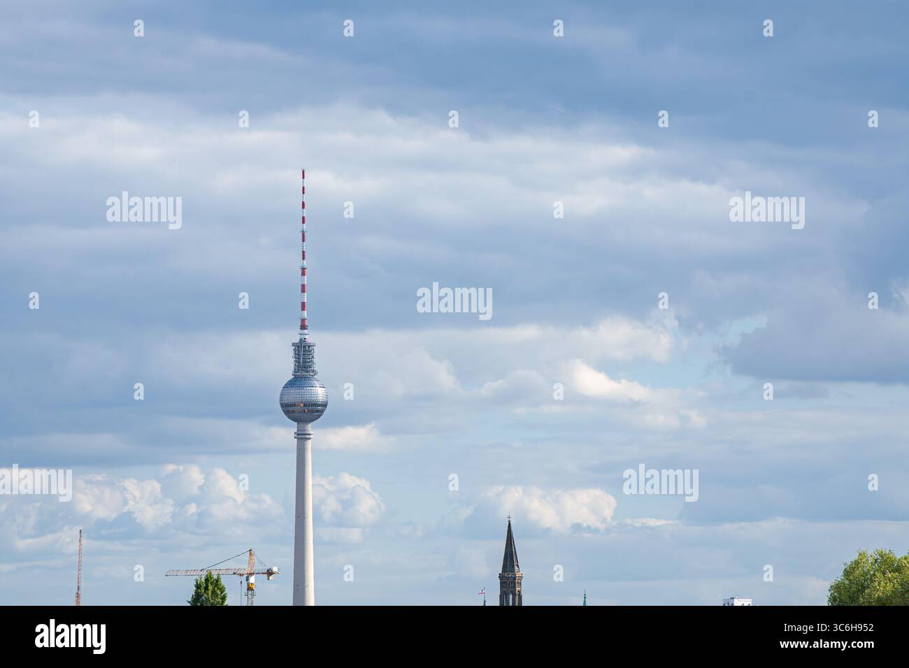 Una lontana vista diurna della Torre della televisione di Berlino (Fernsehturm), incorniciata contro un cielo dinamico pieno di nuvole testurizzate. Foto Stock