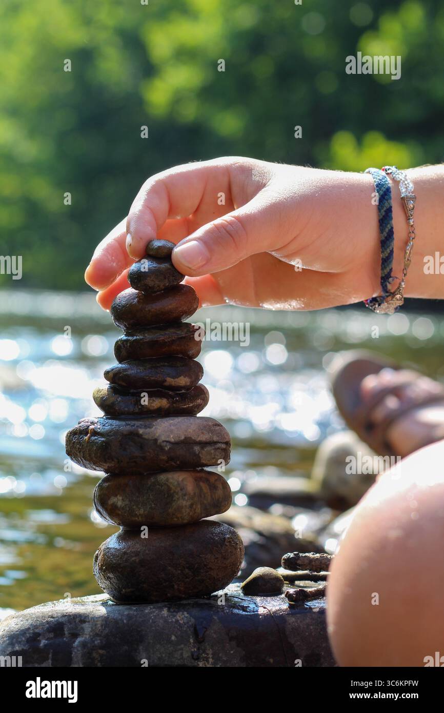 Primo piano di Hands Stacking Rocks by a Stream in un tranquillo ambiente naturale Foto Stock