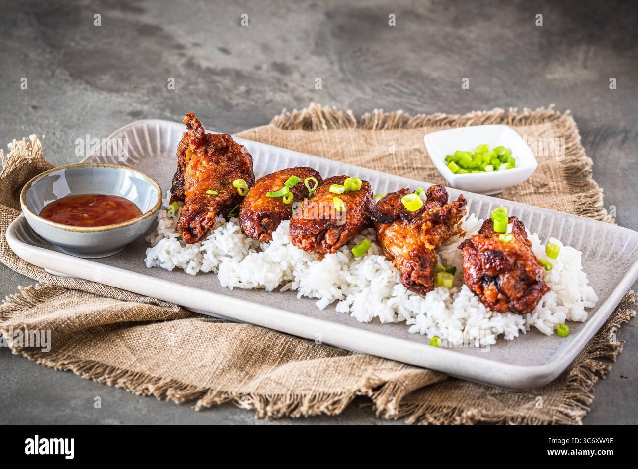 Ali di pollo fritte in profondità con salsa sul riso su fondo rustico in cemento grigio, copia spazio Foto Stock
