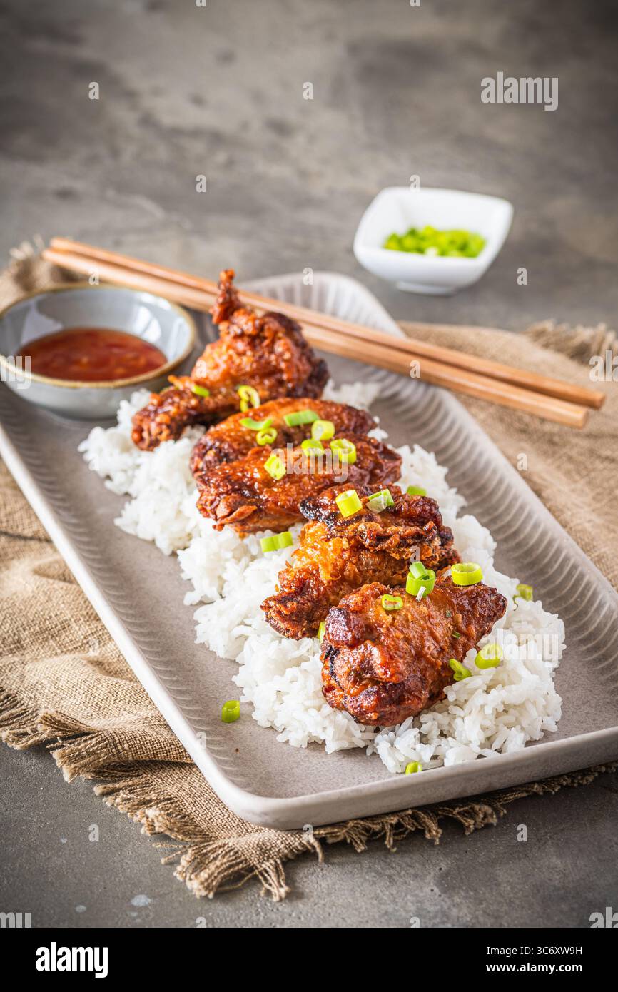 Ali di pollo fritte in profondità con salsa sul riso su fondo rustico in cemento grigio, verticale con spazio di copia Foto Stock