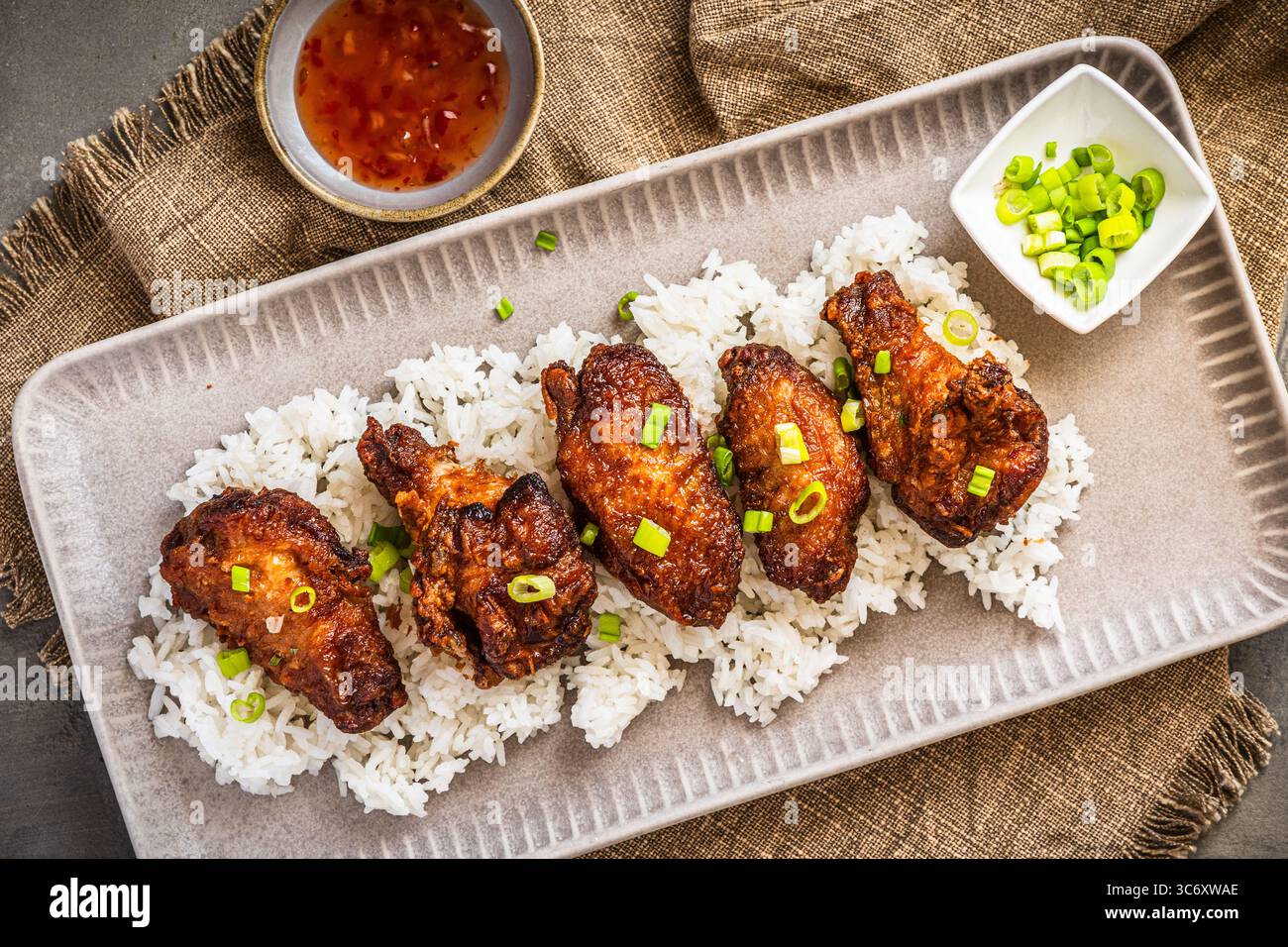Ali di pollo fritte in profondità con salsa sul riso su fondo rustico in cemento grigio, vista dall'alto Foto Stock