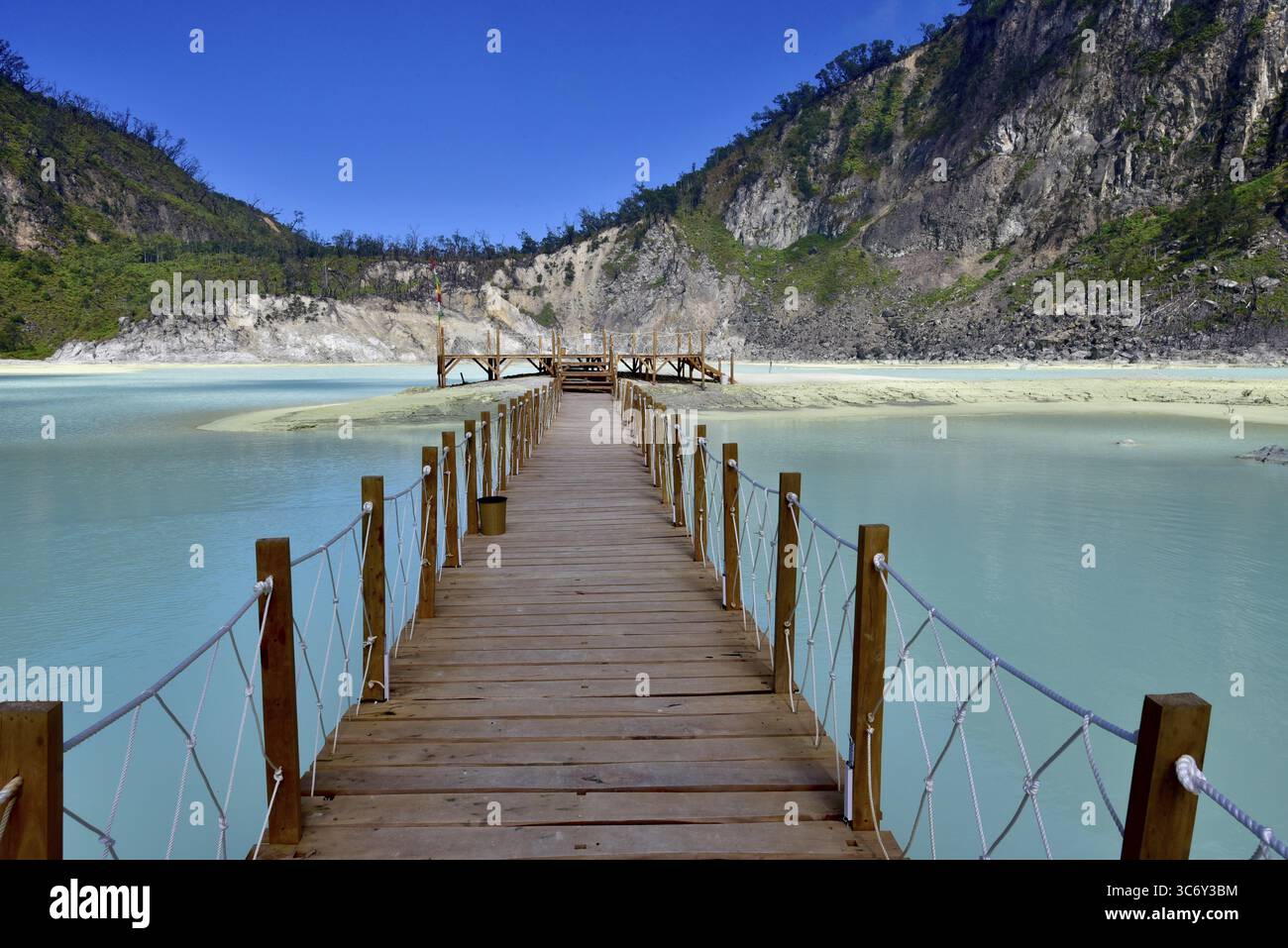 Una passerella in legno conduce su un lago sulfuroso di colore turchese circondato da verdi montagne, Kawa Putih, Bandung, Giava, Indonesia Foto Stock