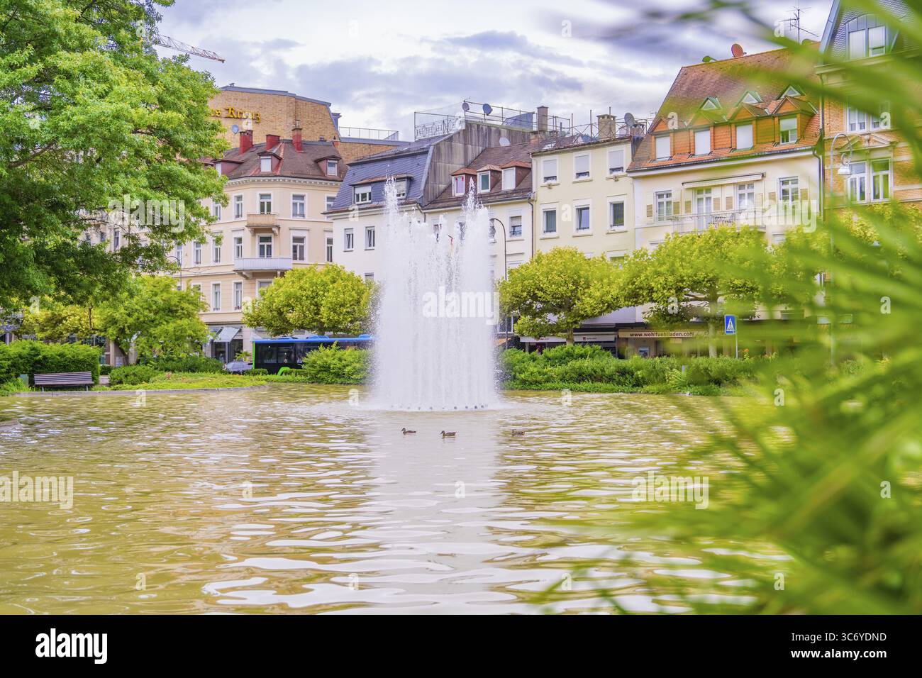 Una fontana in uno stagno urbano, circondata da edifici e vegetazione verde, Baden Baden, Germania Foto Stock
