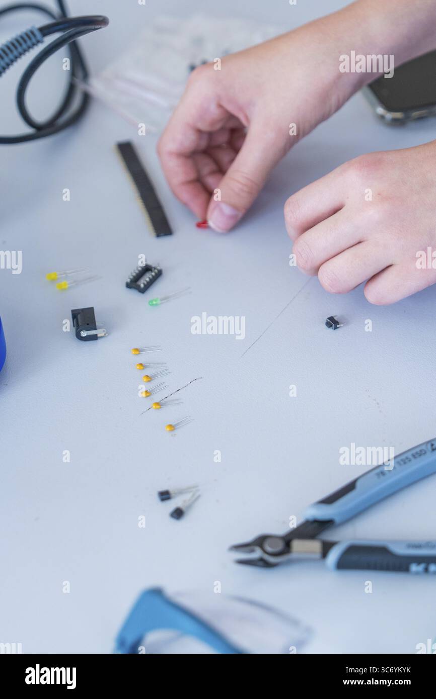 Mani che lavorano con piccoli componenti elettronici e utensili su un tavolo Foto Stock