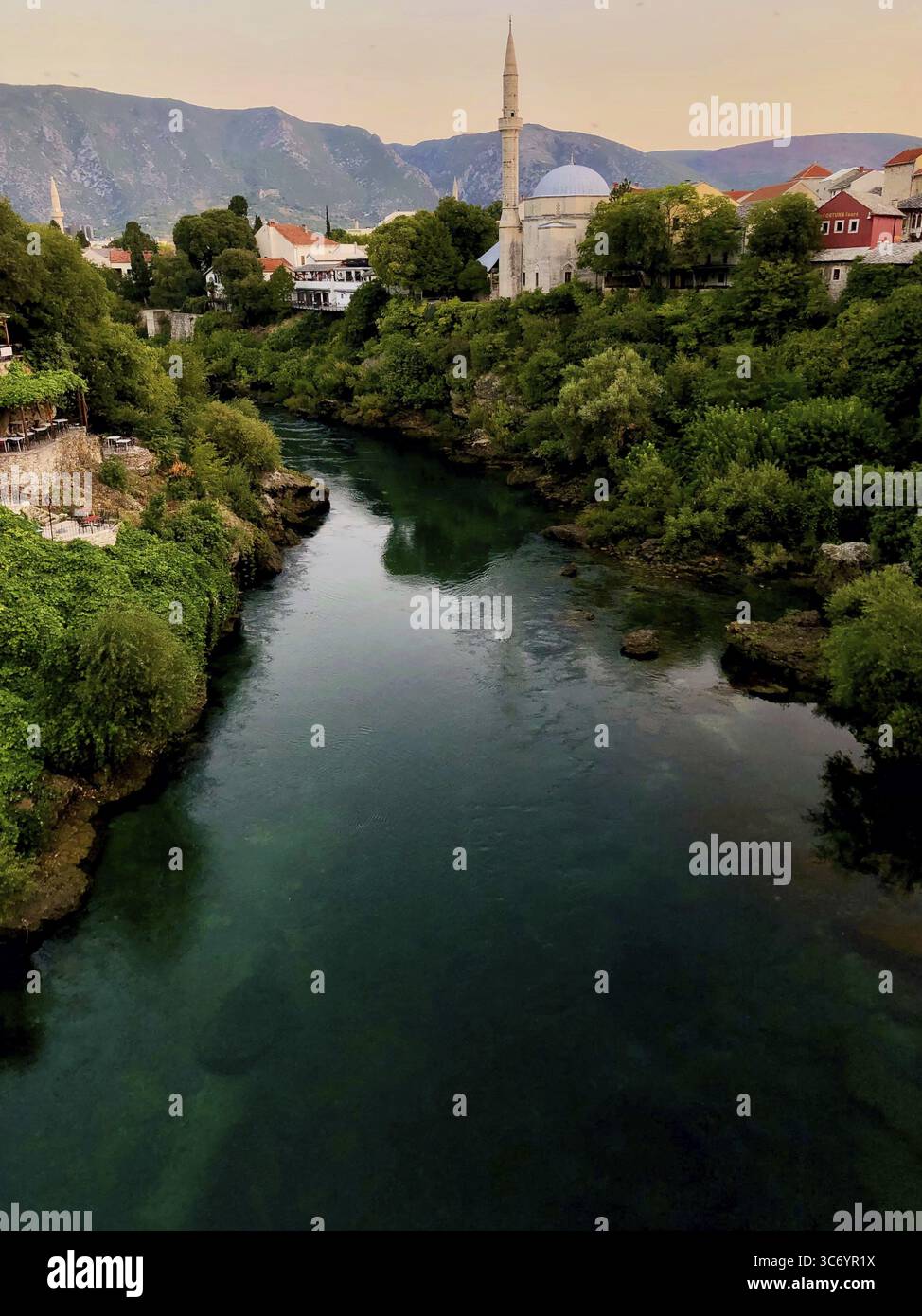 Fiume in una città con un minareto e vegetazione lussureggiante al crepuscolo, Mostar, Bosnia ed Erzegovina Foto Stock