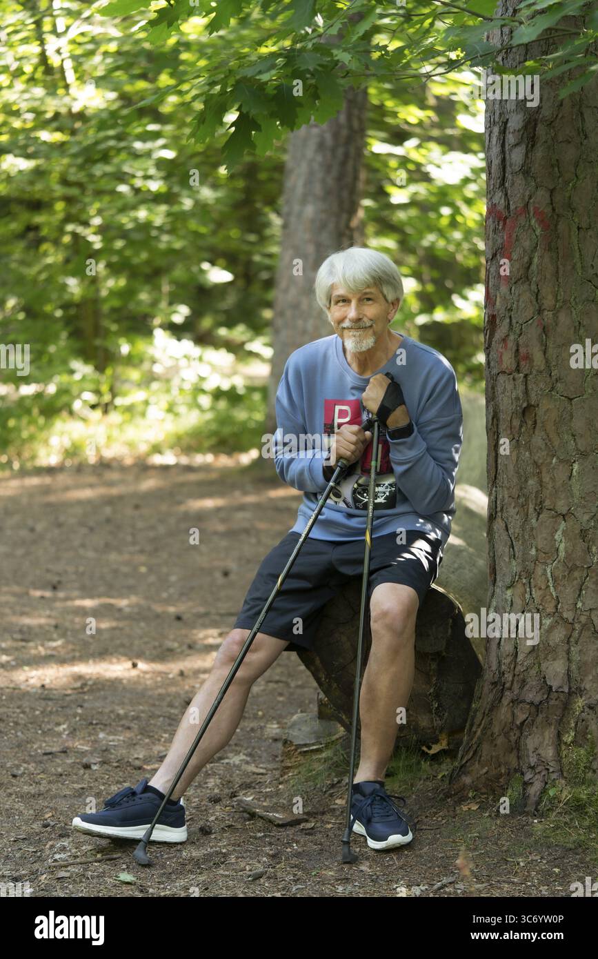 In forma, l'uomo anziano siede con bastoncini da passeggio su un fascio nella foresta, TRIMM dich Path Foto Stock
