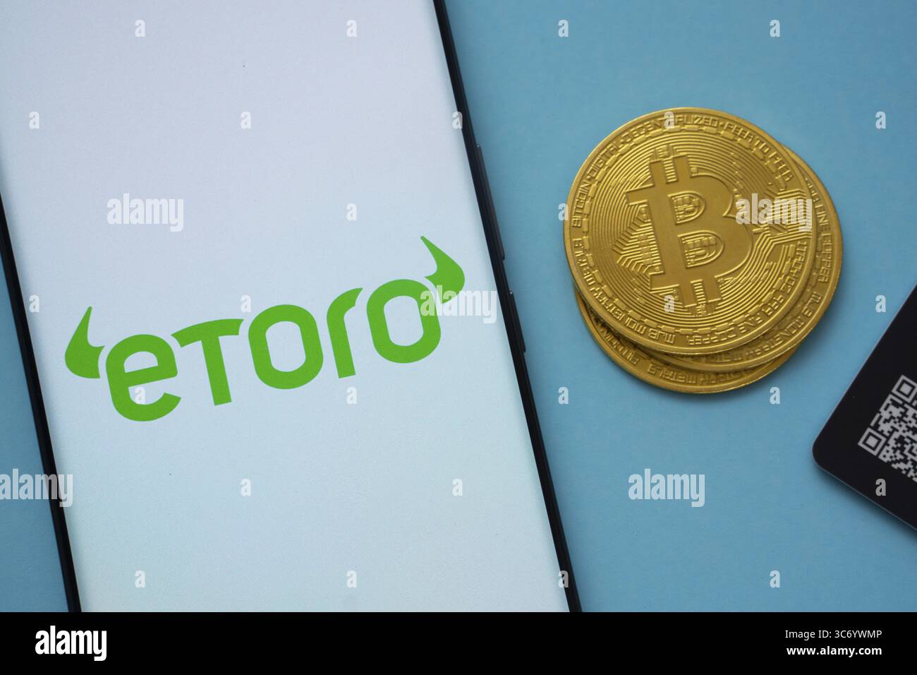 Dhaka, Bangladesh - 22 giugno 2025: Logo eToro sullo schermo dello smartphone vicino alla moneta Bitcoin e codice QR su sfondo blu Foto Stock