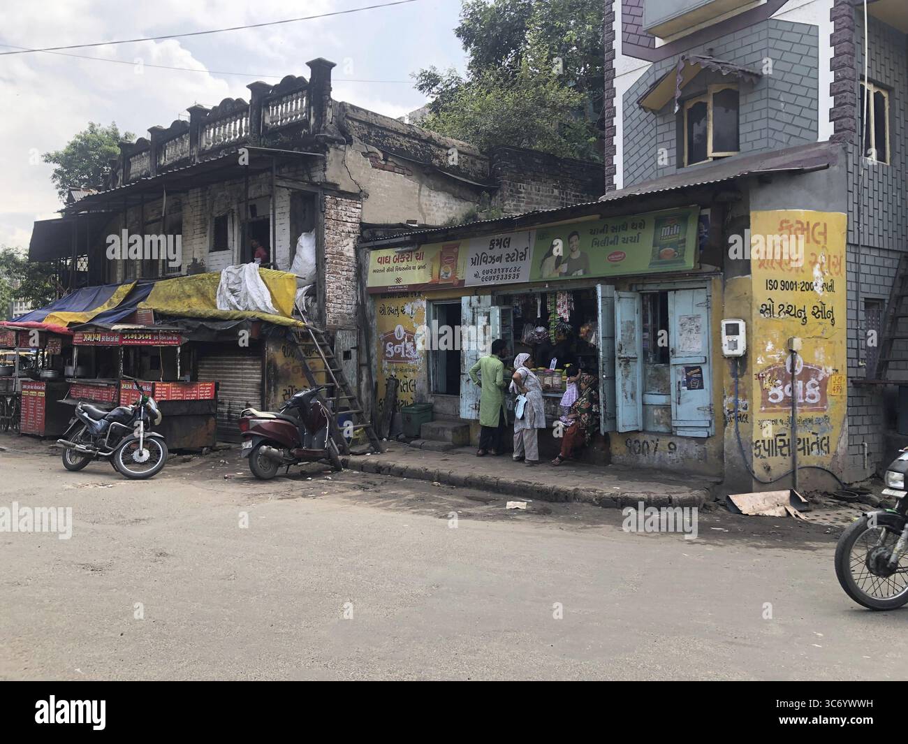 Strada trafficata di fronte a vecchi negozi. Persone in piedi di fronte a piccoli negozi e motociclette parcheggiavano lungo la strada, Ahmedabad, Gujarat, India Foto Stock