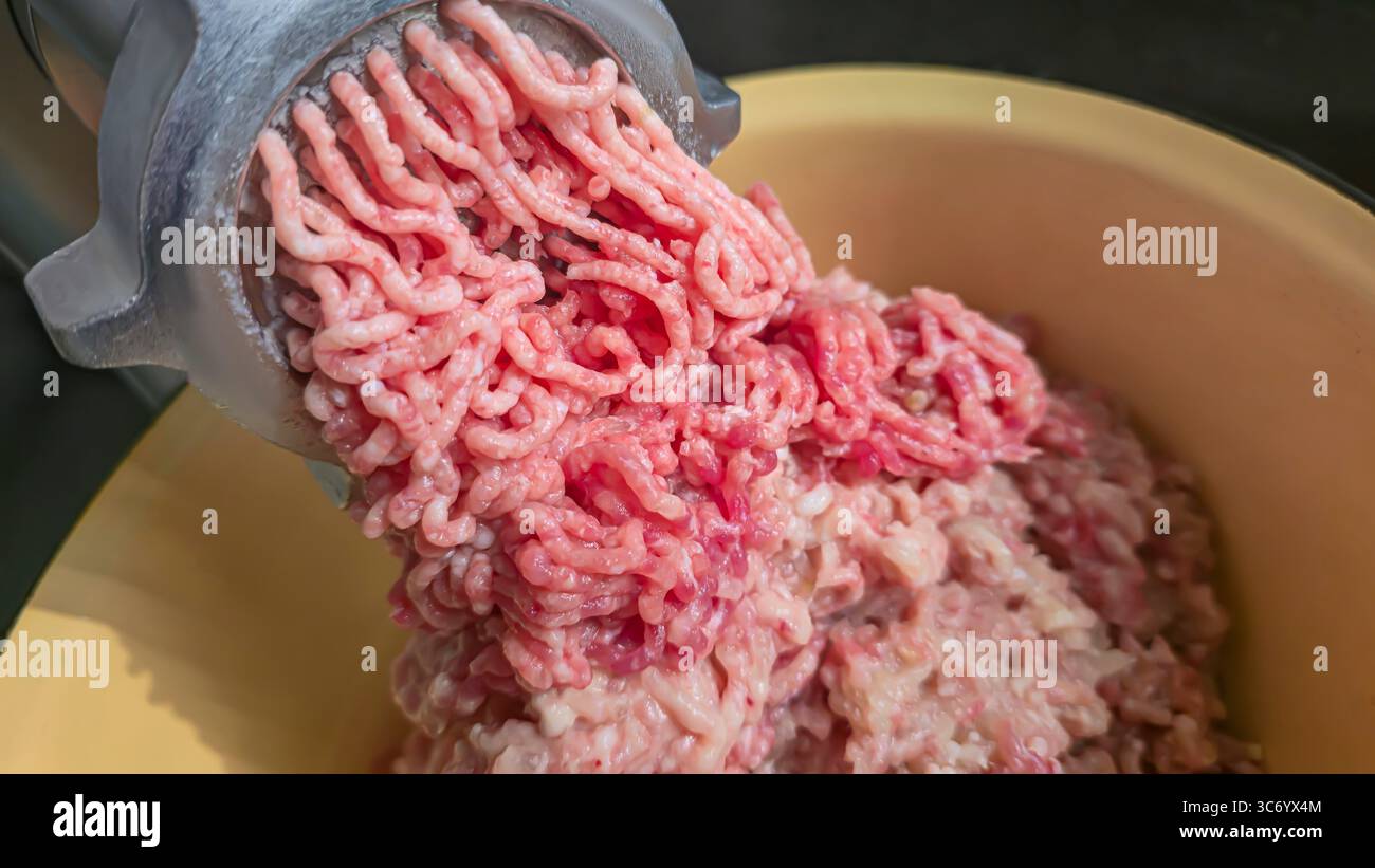 Macinacaffè con carne macinata fresca sul tavolo della cucina. Primo piano della carne macinata che cade in un recipiente di metallo. Messa a fuoco selettiva. Foto Stock